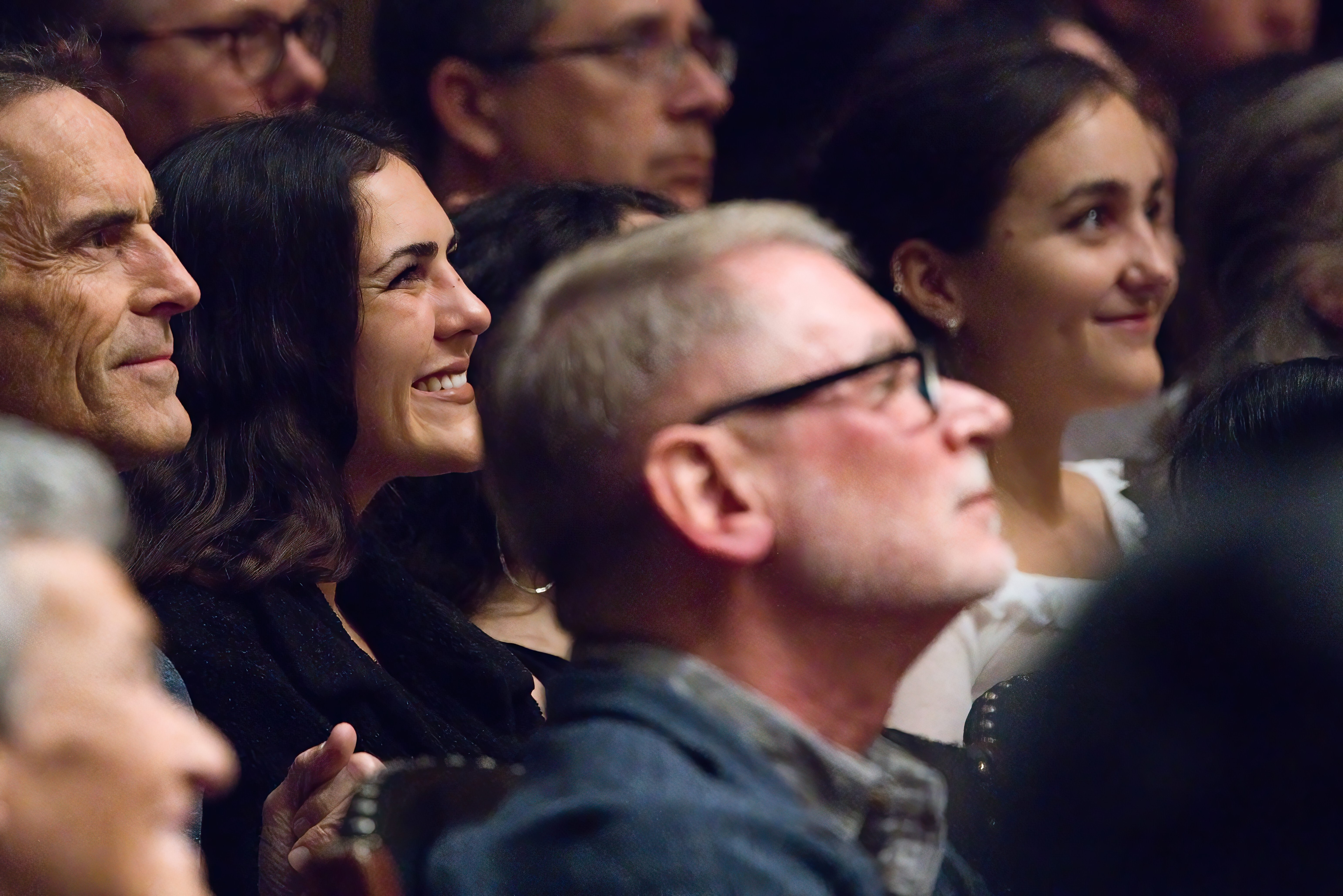 Audience members smiling in symphony hall looking up to the stage.