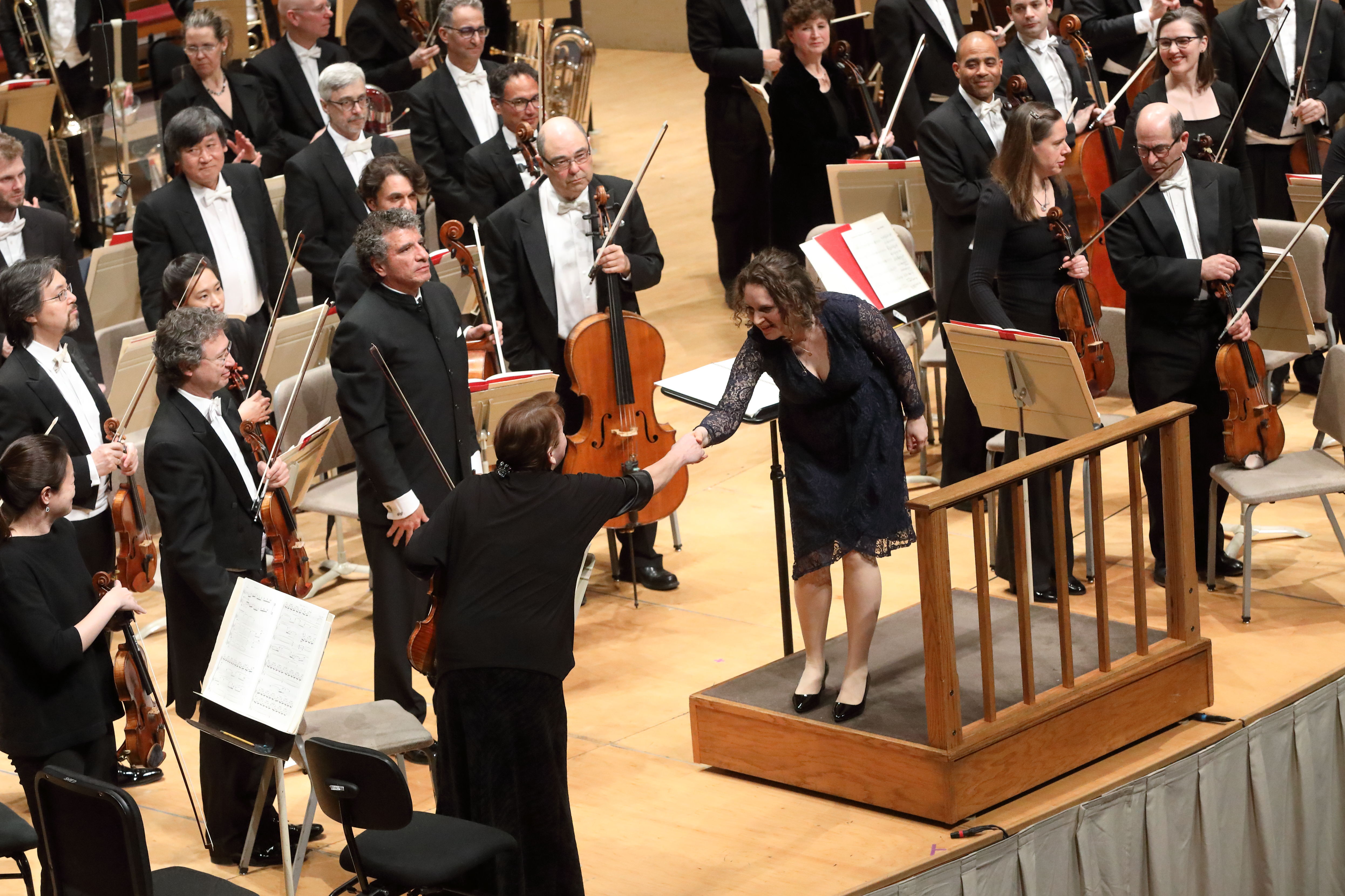 A woman bows and shakes the hand of the concertmaster standing to her left.