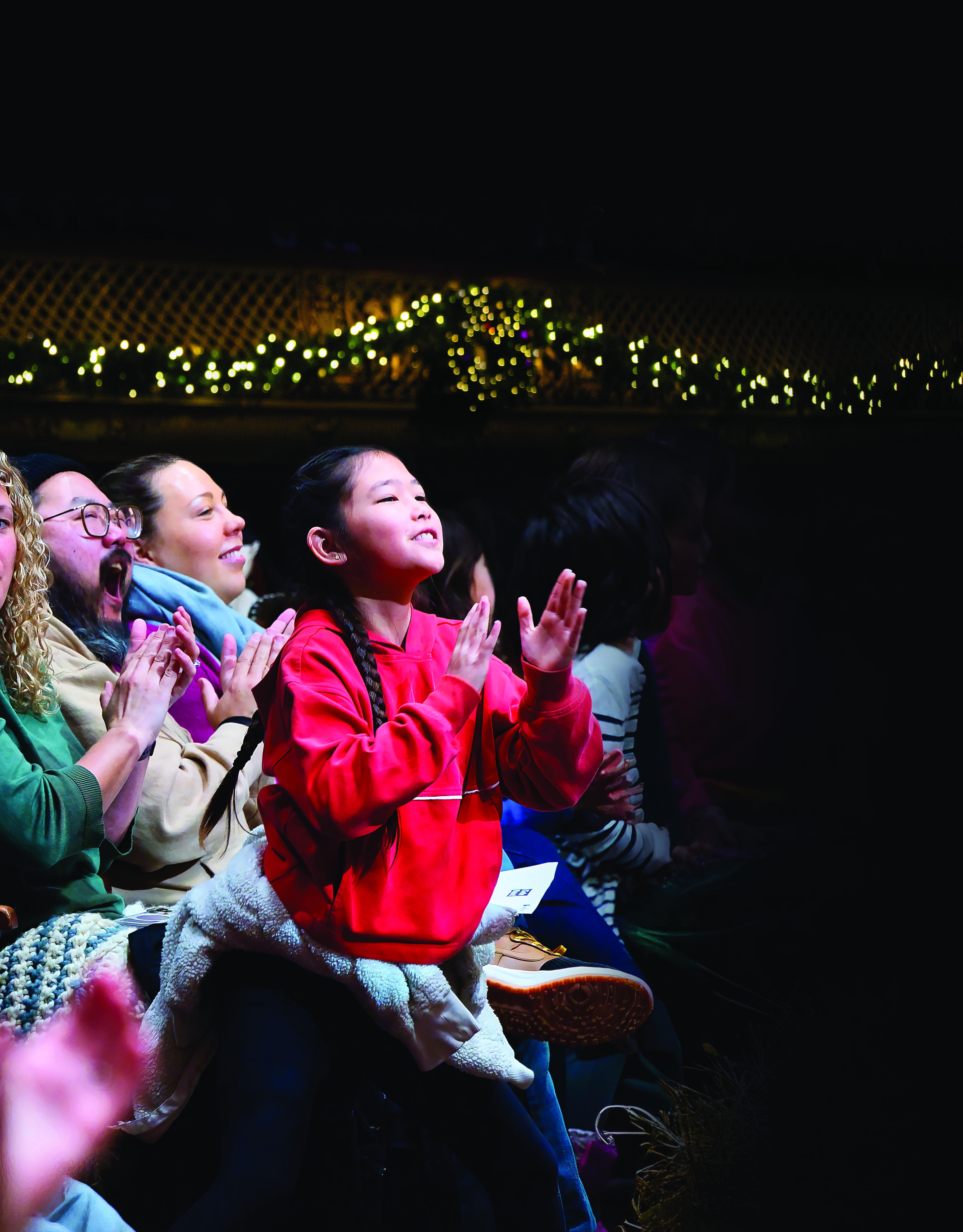 a young child smiles and applauds looking up at the stage