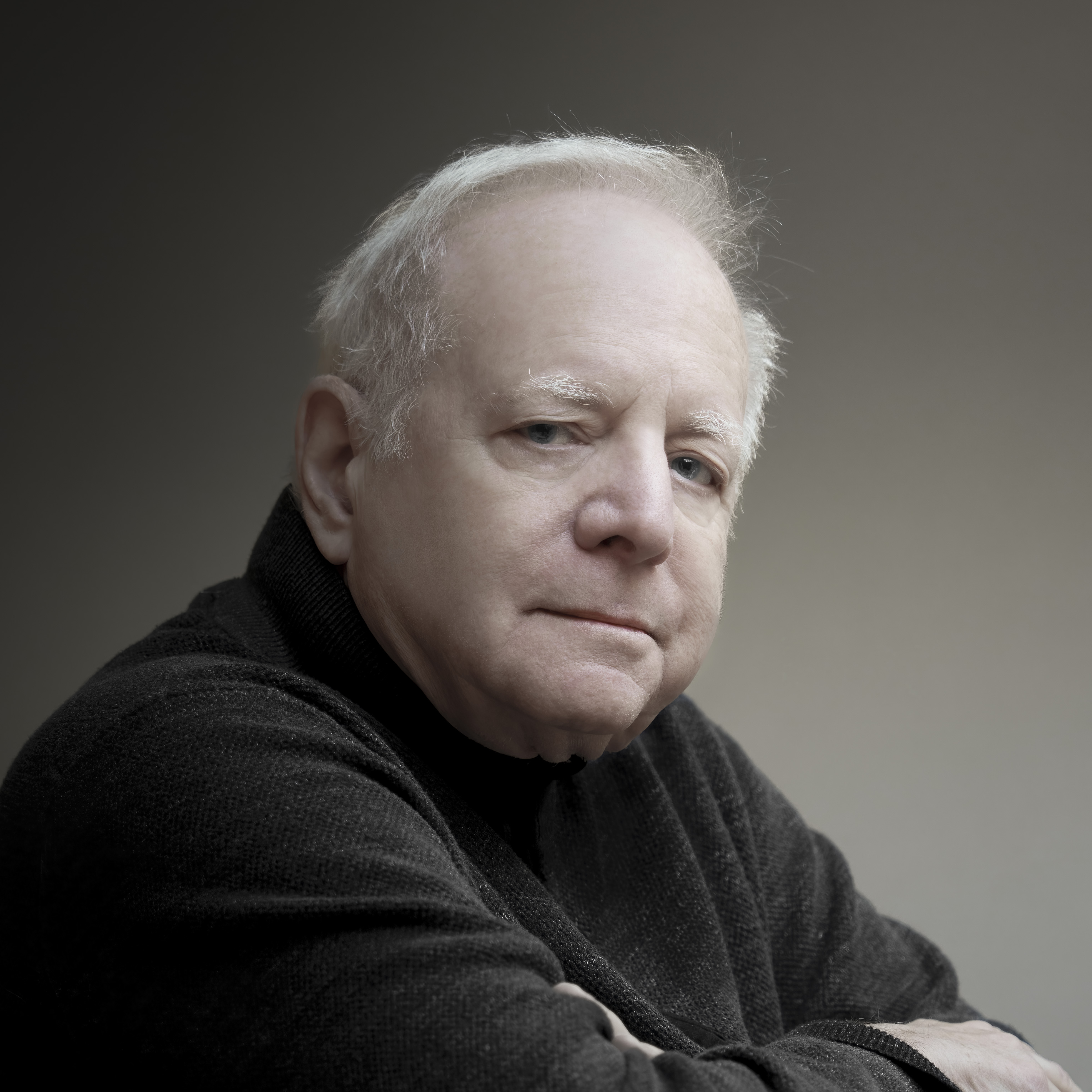 Leonard Slatkin wearing a dark sweater sitting with his arms crossed and looking at the camera.