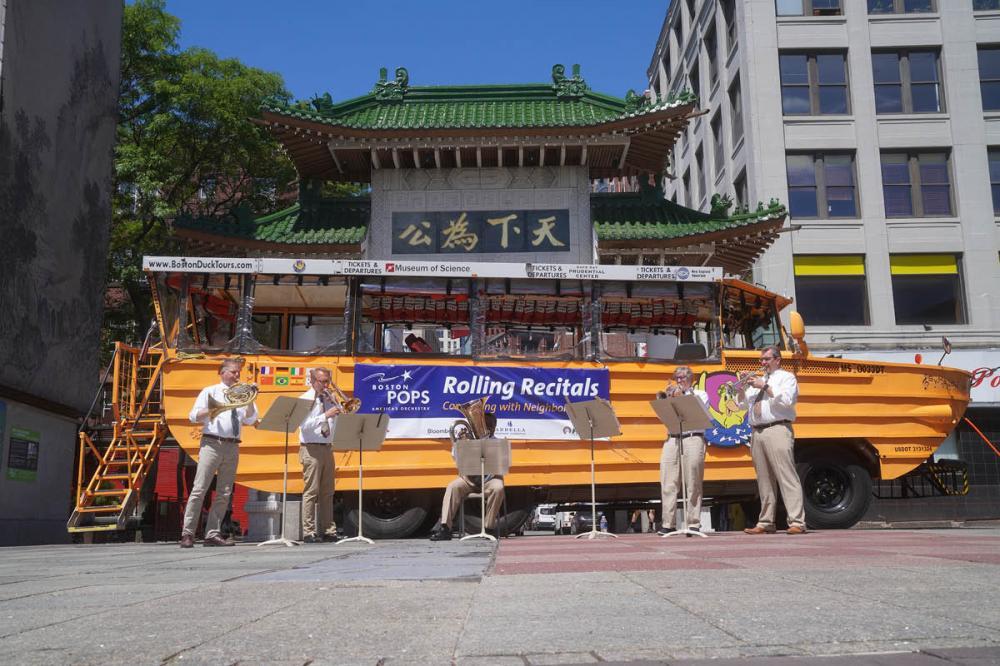 A brass band performs in front of a duck boat.