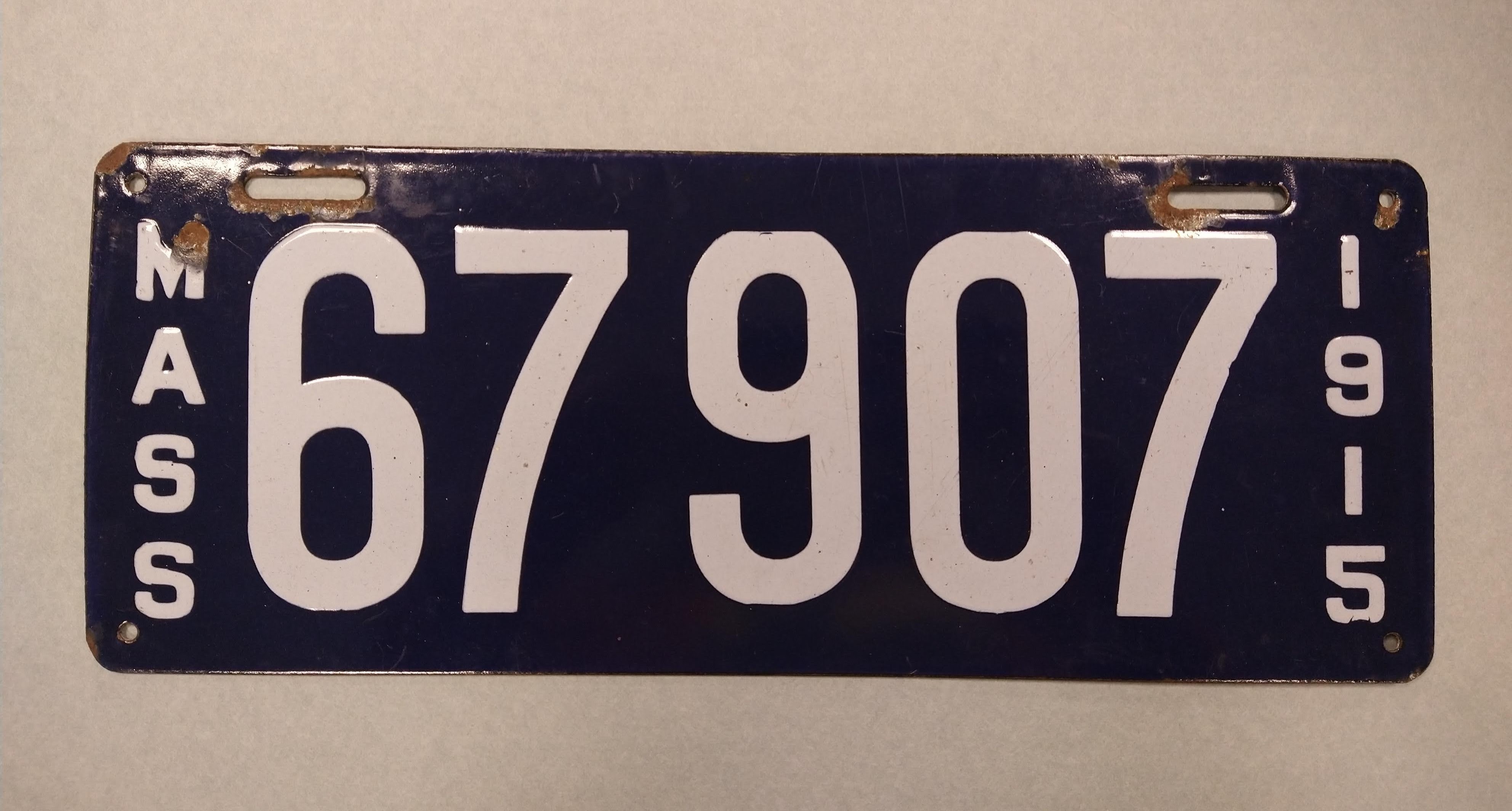 Dark blue plate dated 1915, state-issued license plate from Massachusetts with the numbers 67907