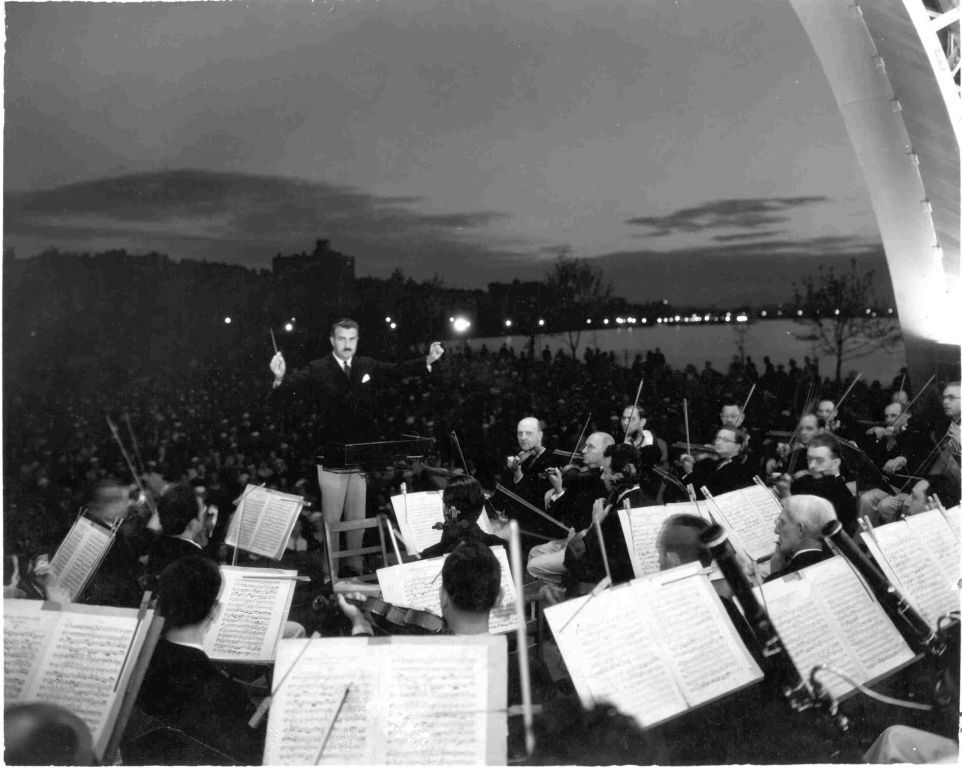 A black and white photo of Arthur Fiedler conducting the Pops at the Hatch Shell on the Charles River Esplanade