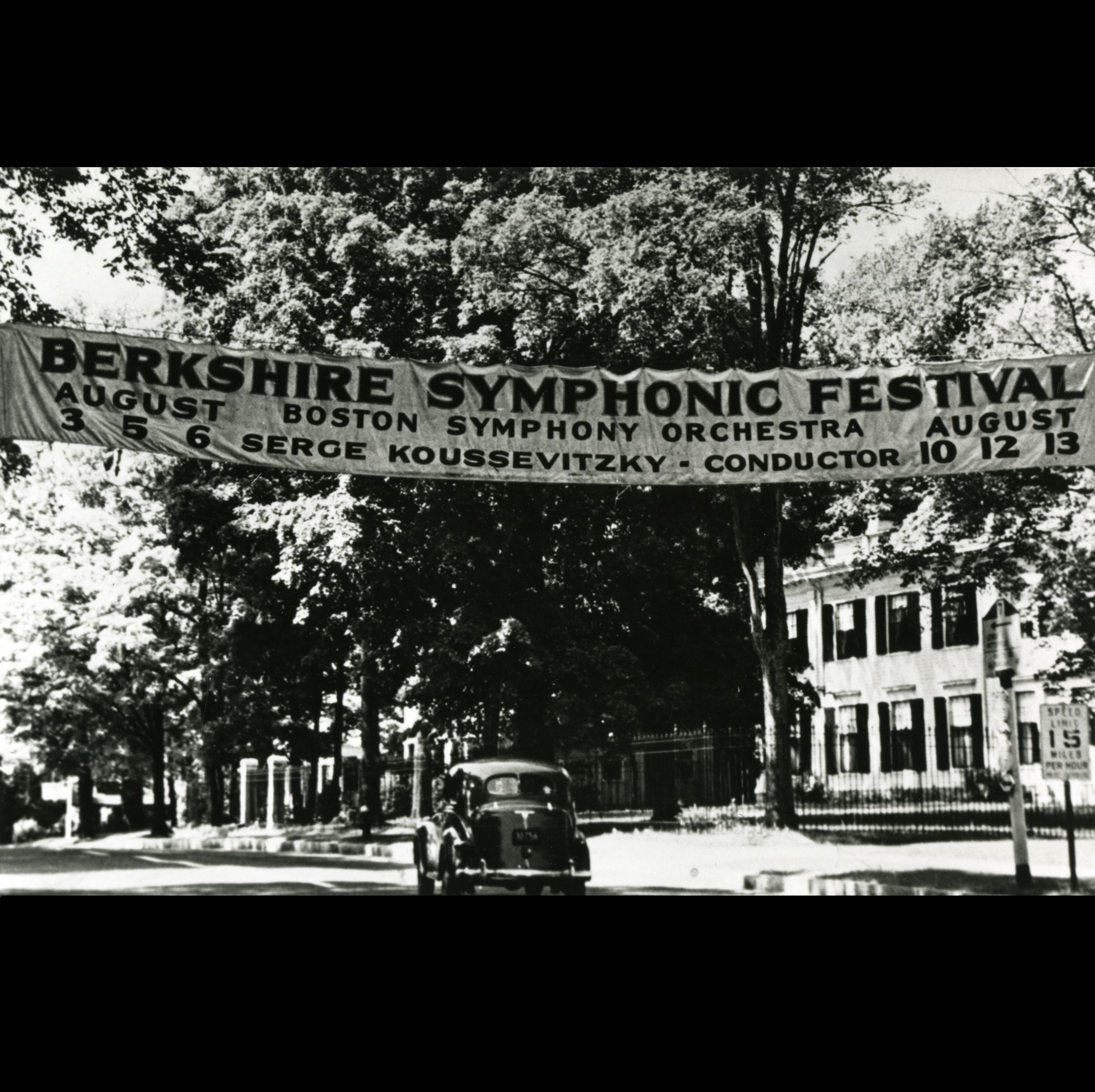 A banner announcing the 1939 Berkshire Symphonic Festival stretches across a tree-lined street with a single automobile on it.