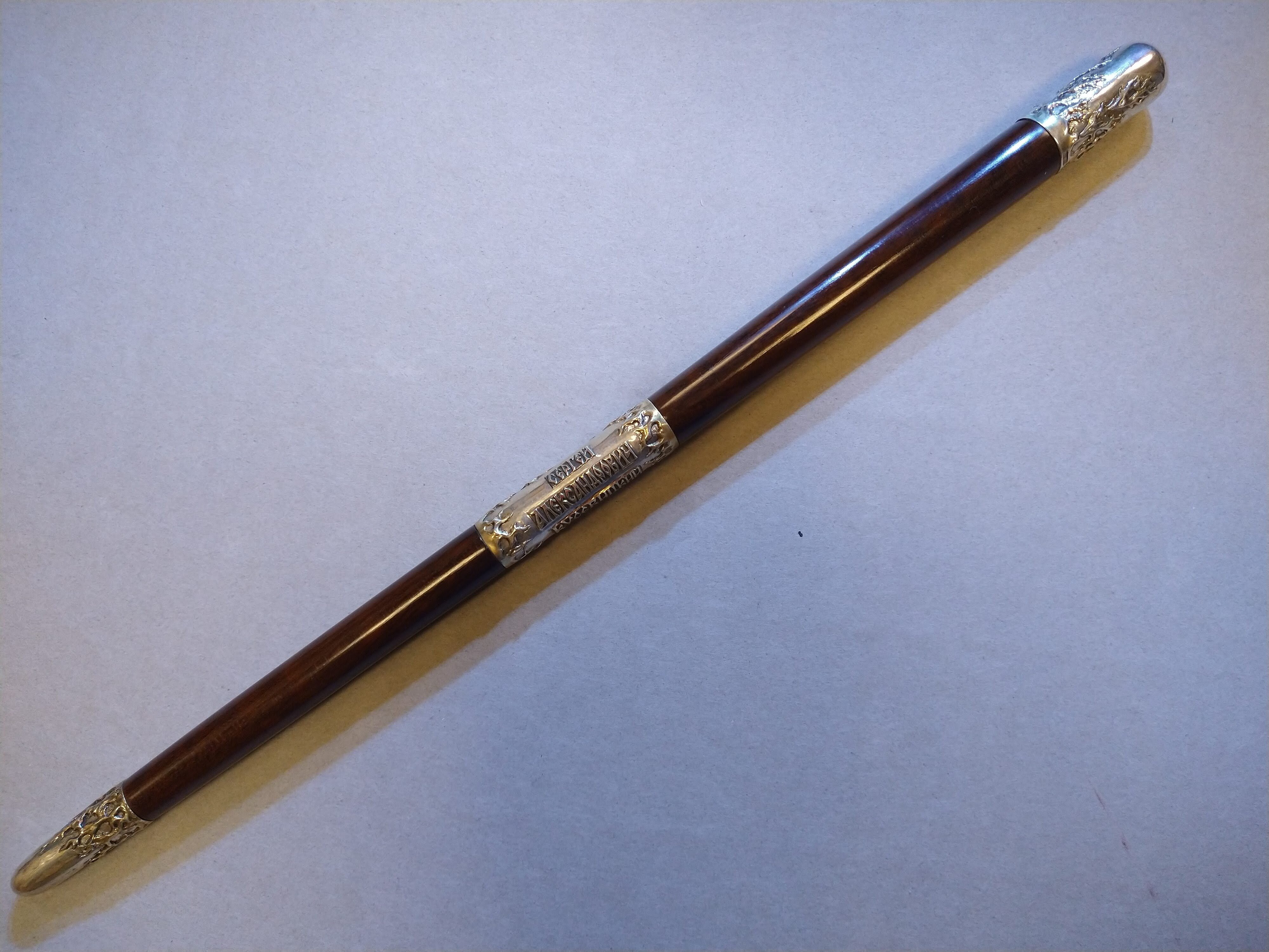 A reddish brown baton with flame engraved metal tips and band inscribed with Serge Alexandrovich Koussevitzky in Cyrillic