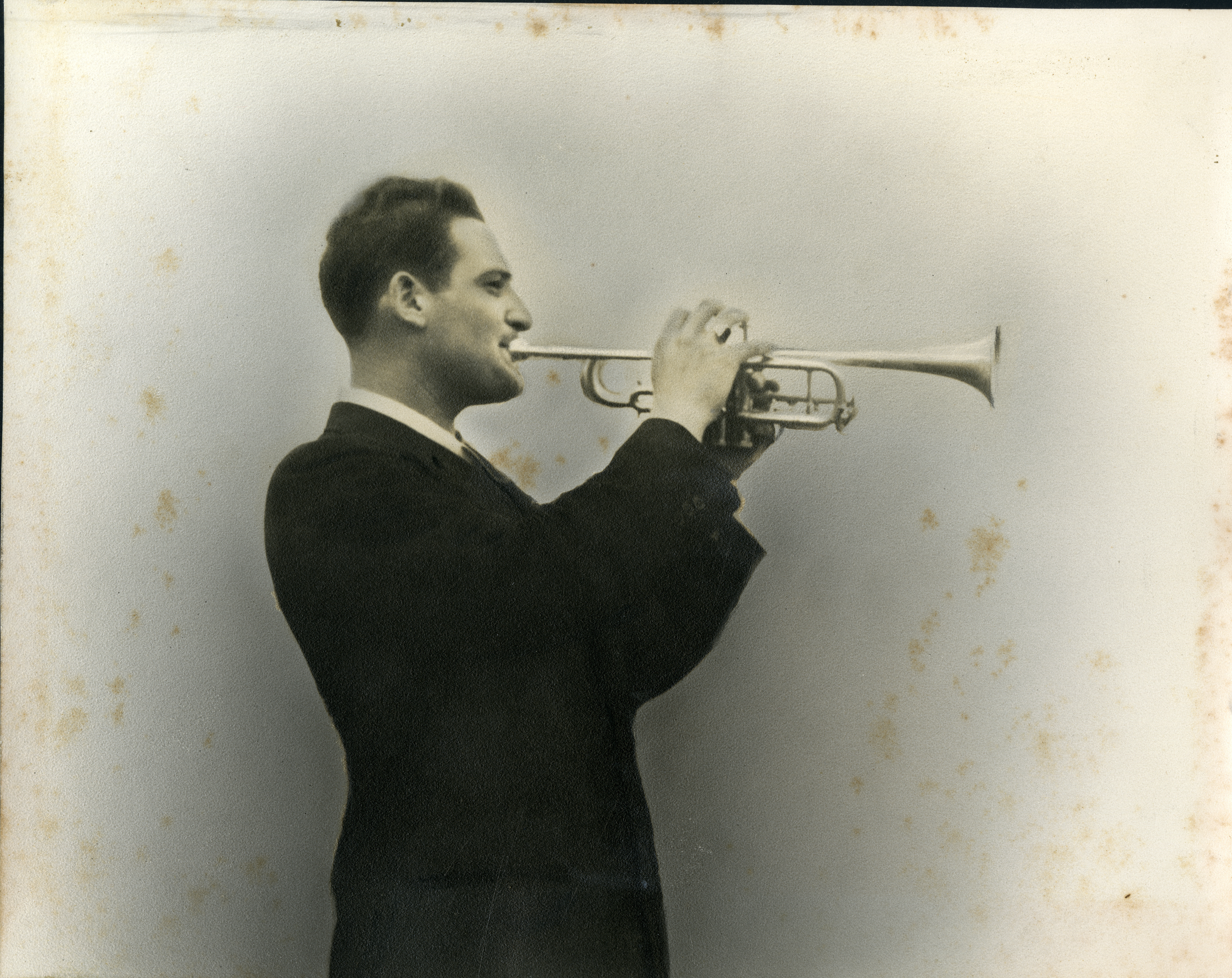 A young man stands in profile holding up a trumpet to his mouth