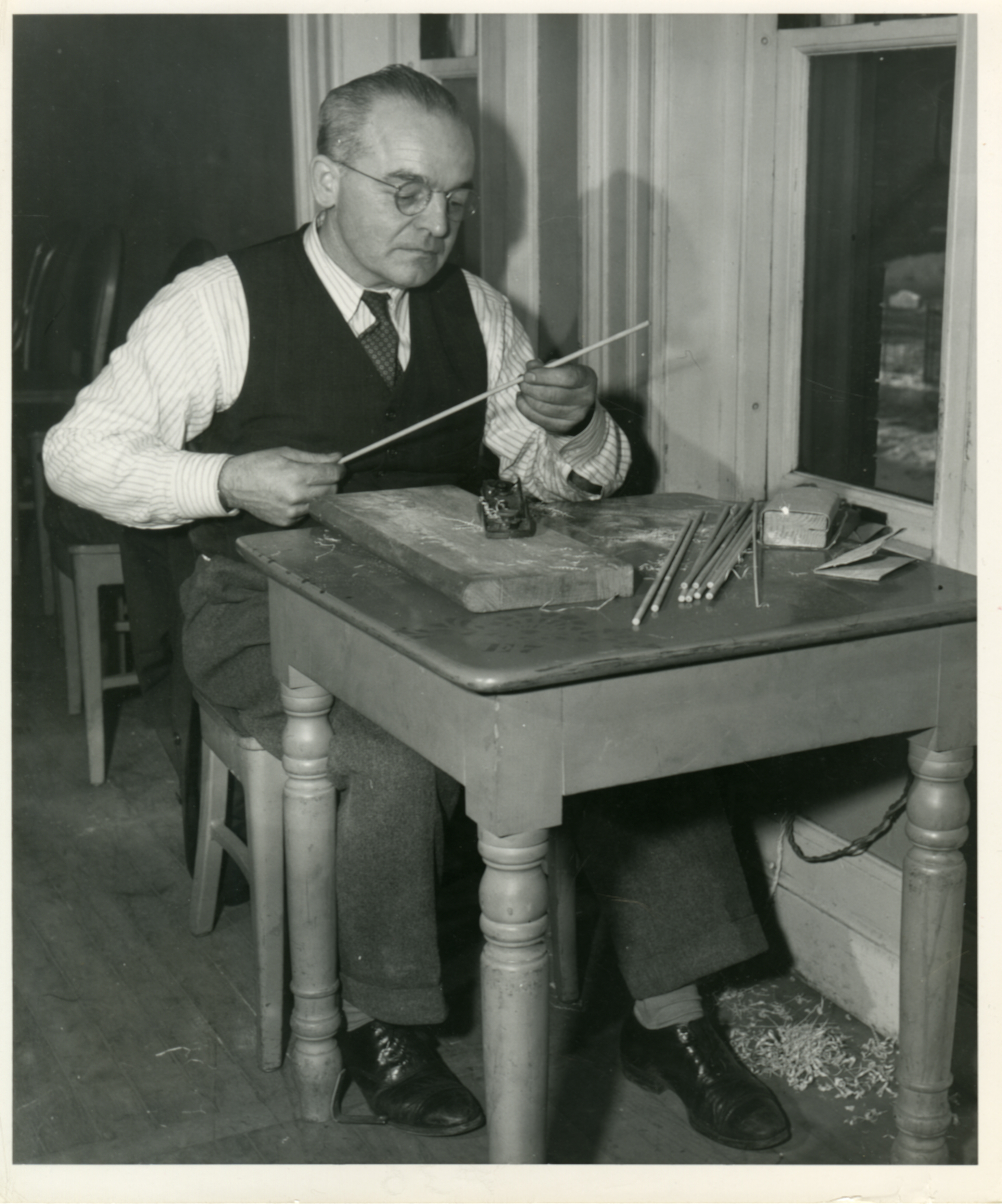 A man sits at a desk holding a wooden towel in process of being made into a baton