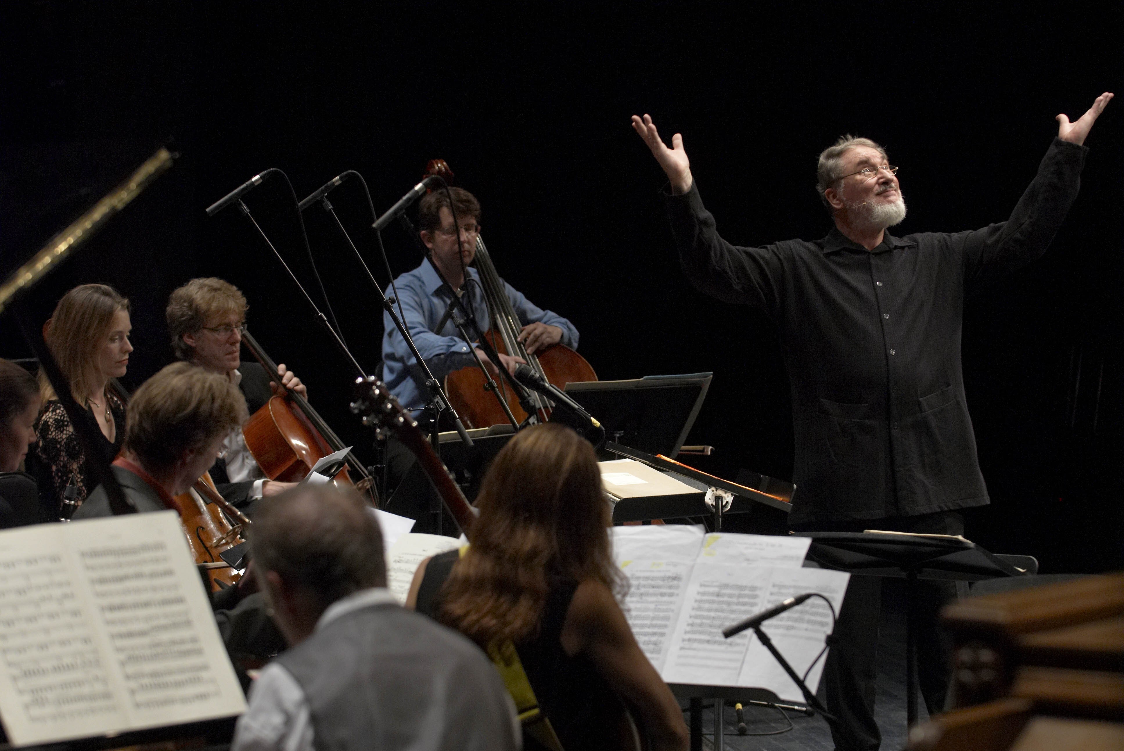 HK Gruber conducting an ensemble with his hands in the air, smiling