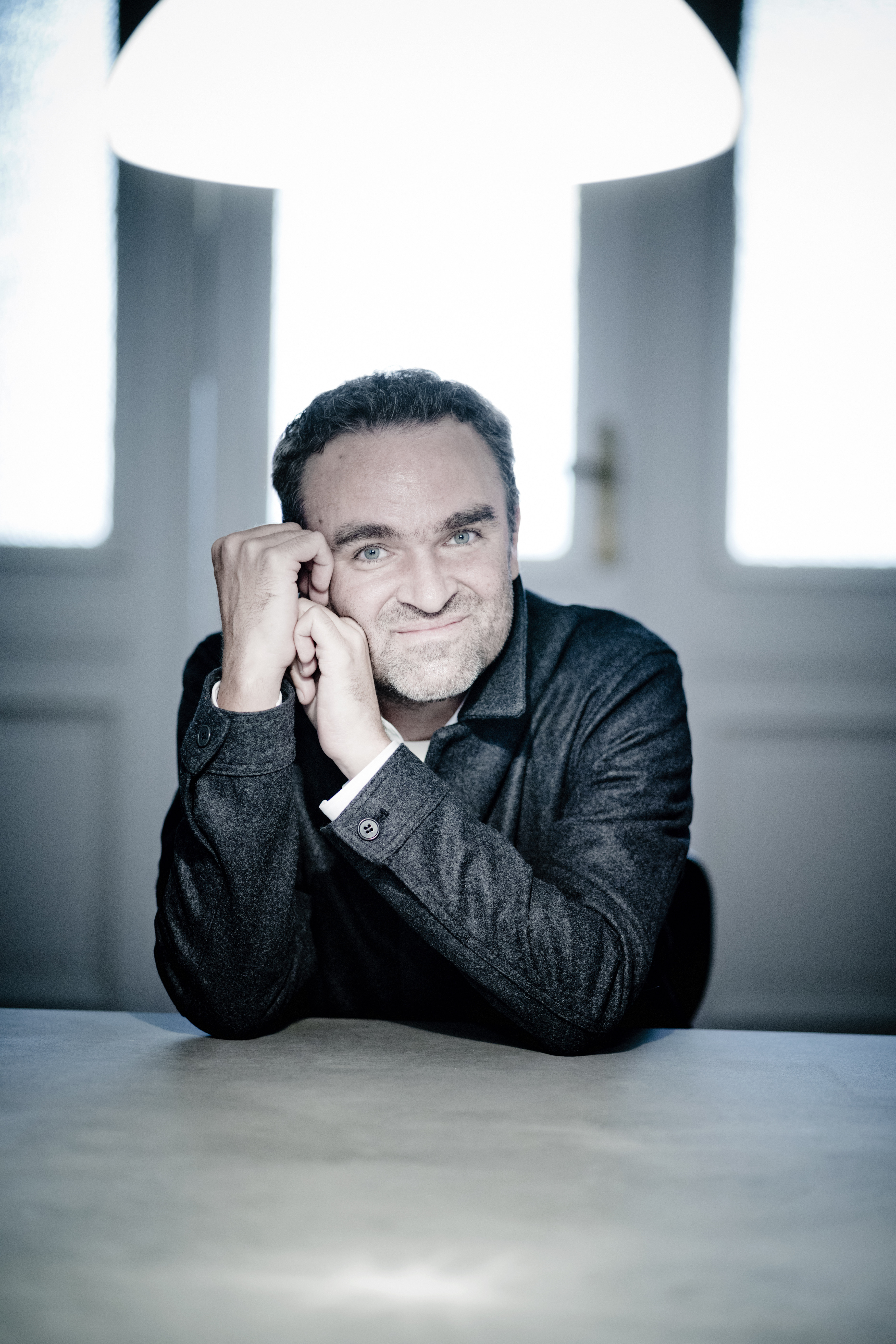Jörg Widmann sitting a table with his hands crossed.