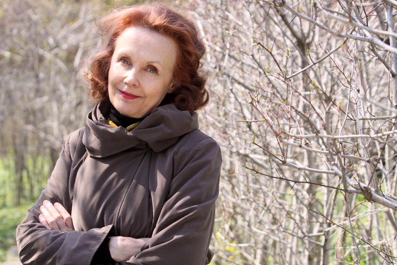 Kaija Saariaho standing outside by some bare trees