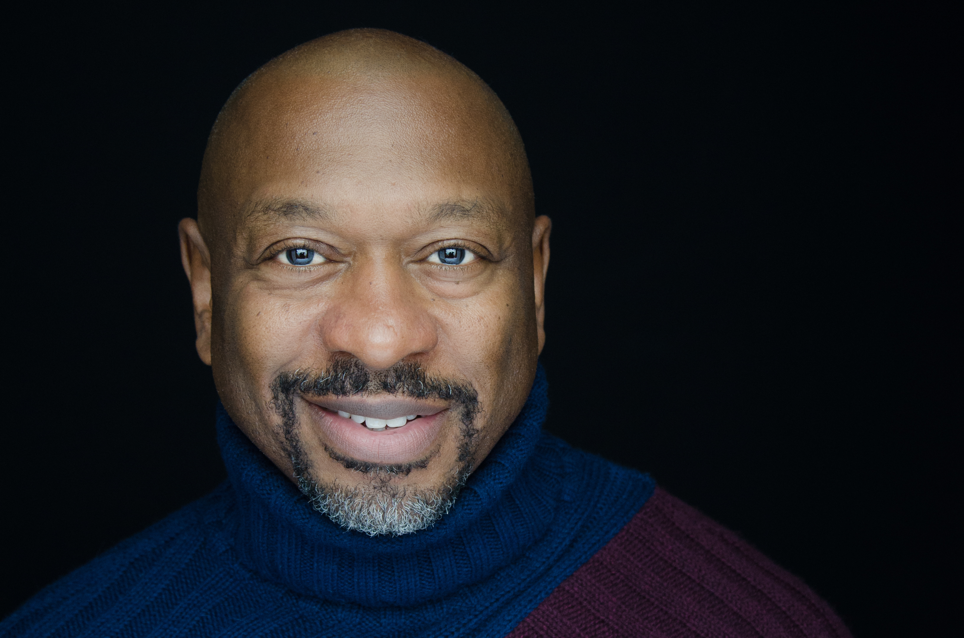 Closeup headshot of smiling man wearing a blue turtleneck sweater