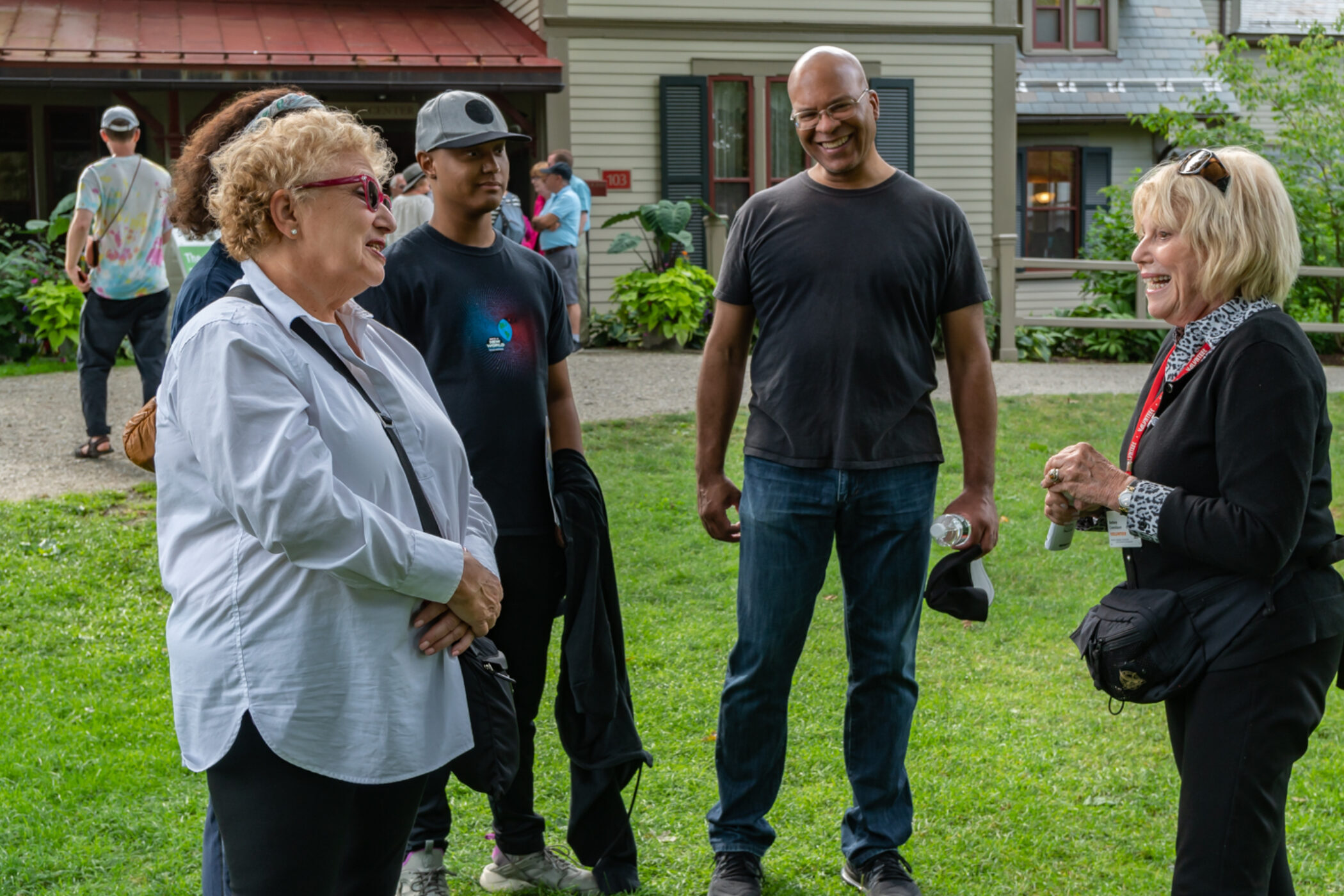 Two women and two men smile and laugh while speaking outside against green grass