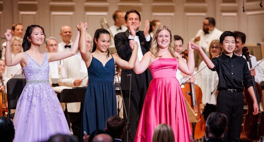 The winners of the 2022 Fidelity Young Artists Competition join hands for a bow on the stage of Symphony Hall in front of Keith Lockhart and the Boston Pops.