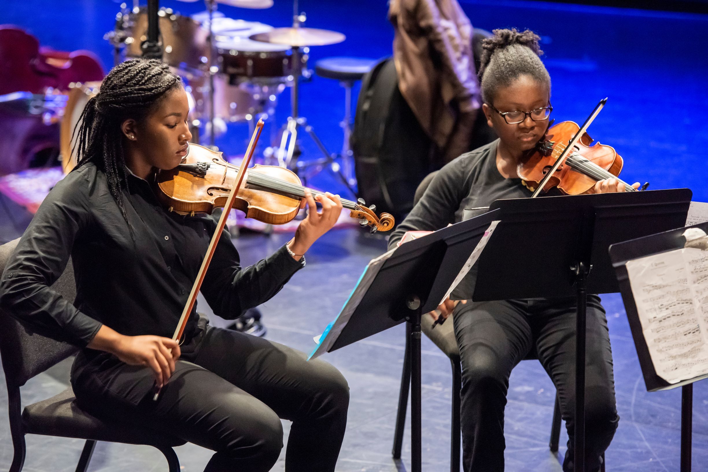 Two musicians, dressed in black, play violins in an ensemble.