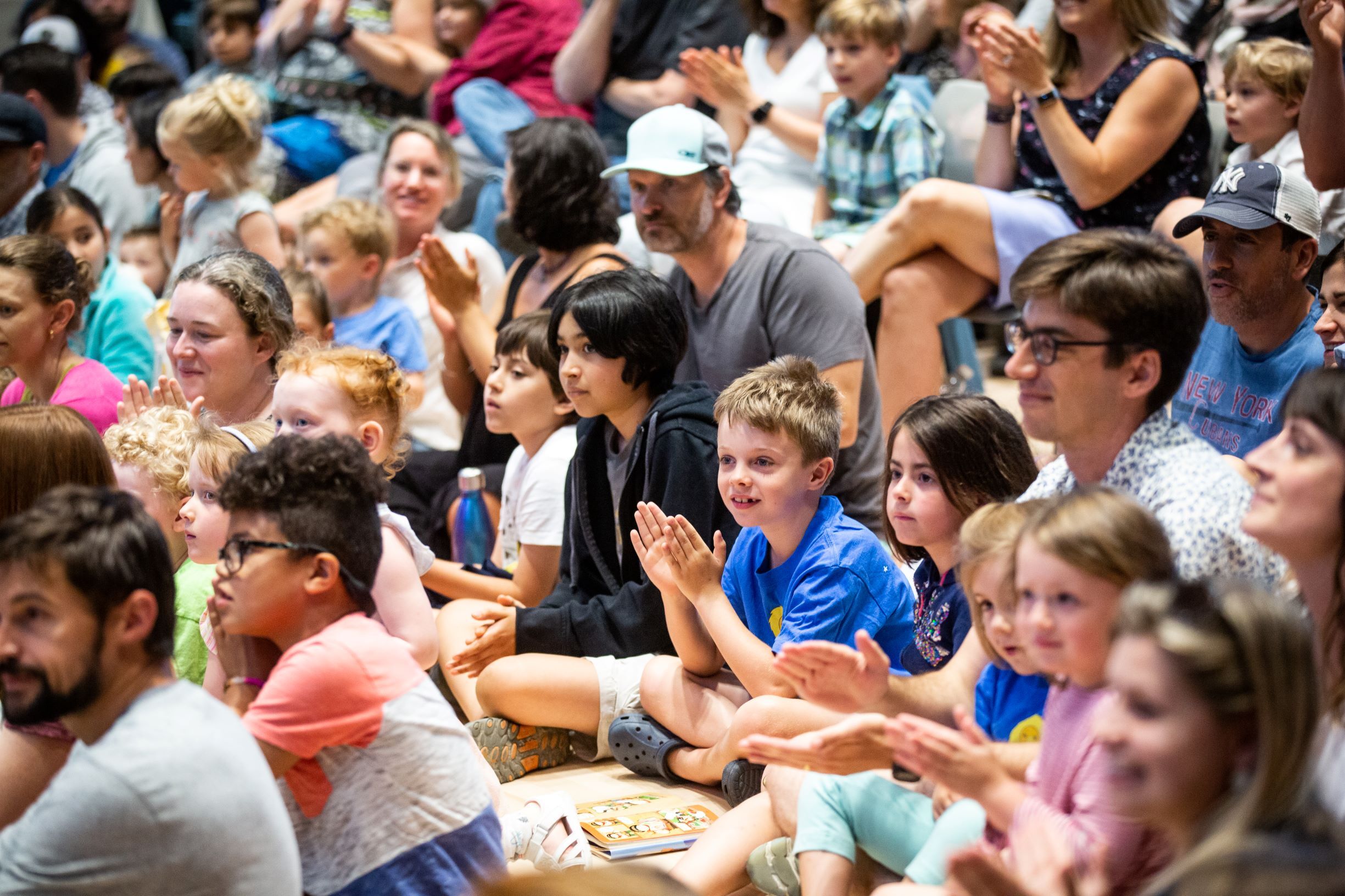 Children and their families sit on the floor and watch a concert.