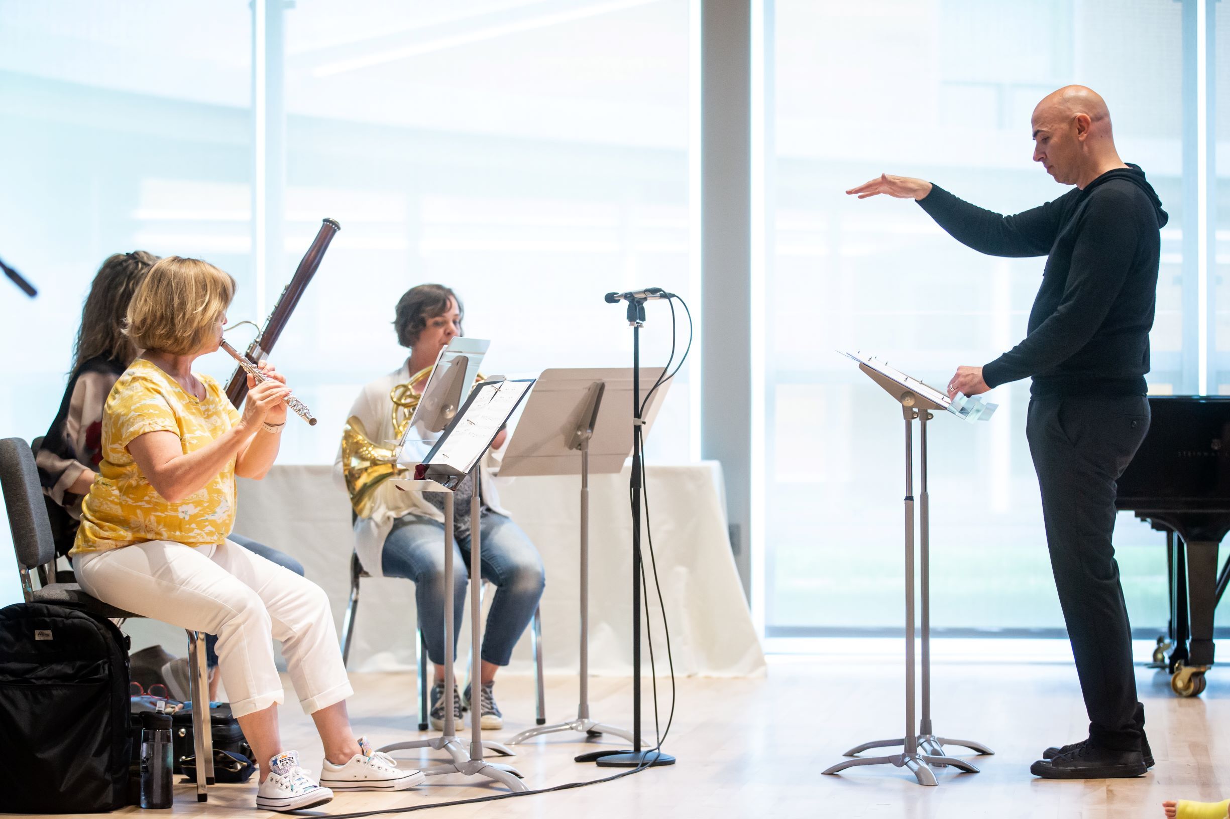A man in black pants and a black sweatshirt conducts a trio of BSO musicians