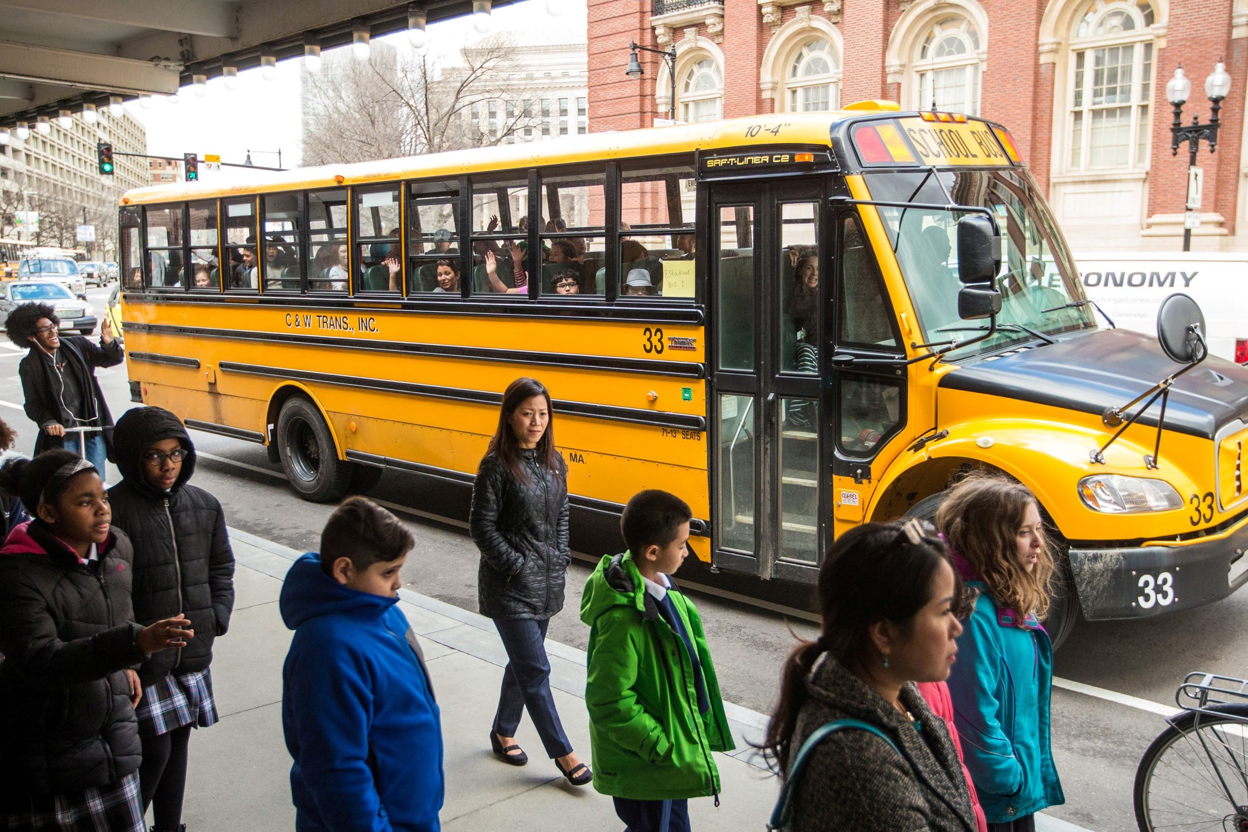 A teacher and students walk near a school bus parked on Massachusetts Avenue.