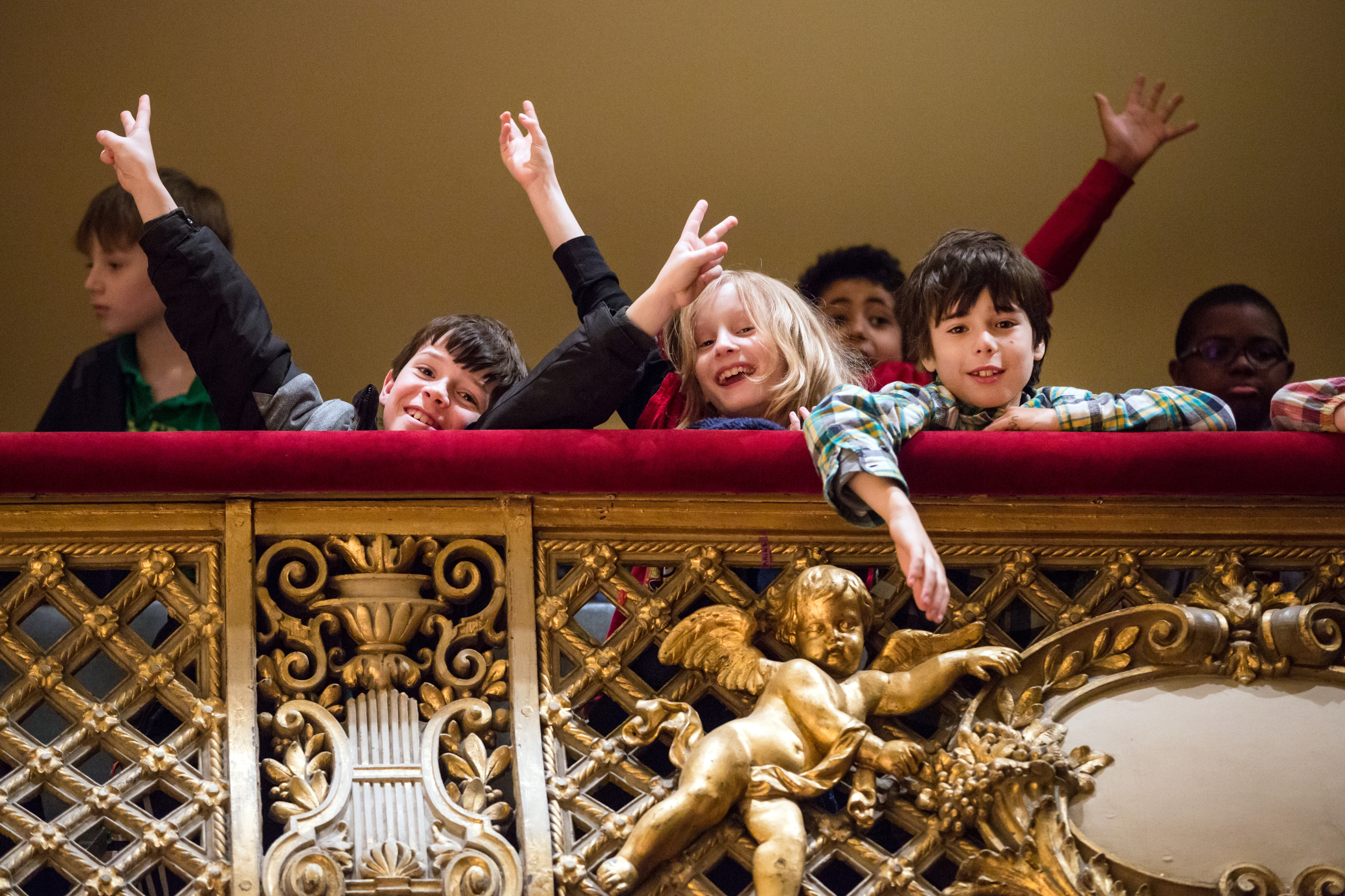 Children standing in a balcony at Symphony Hall posing and throwing their arms up in the air.