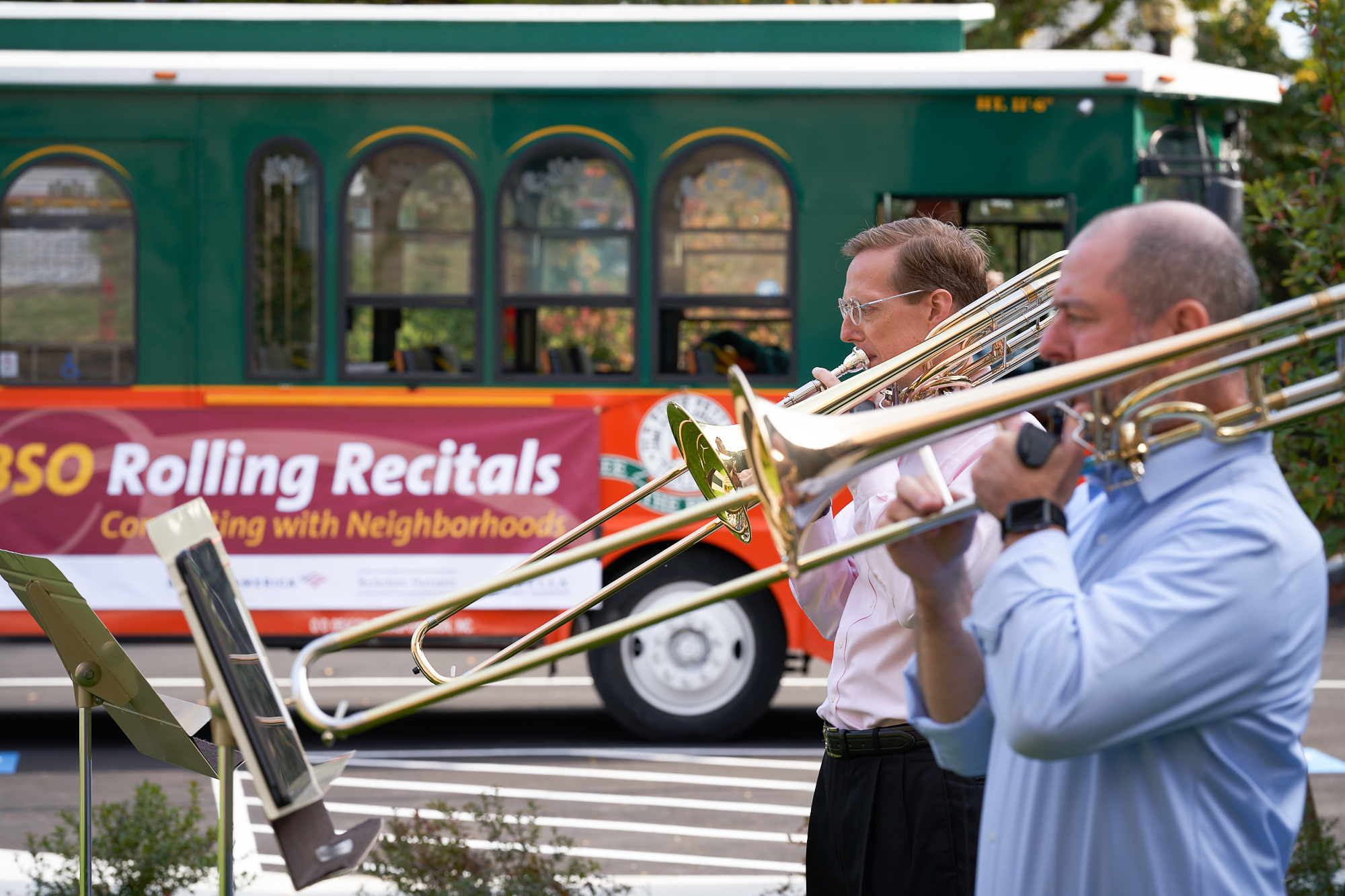 Two men play trombone in front of a trolley.