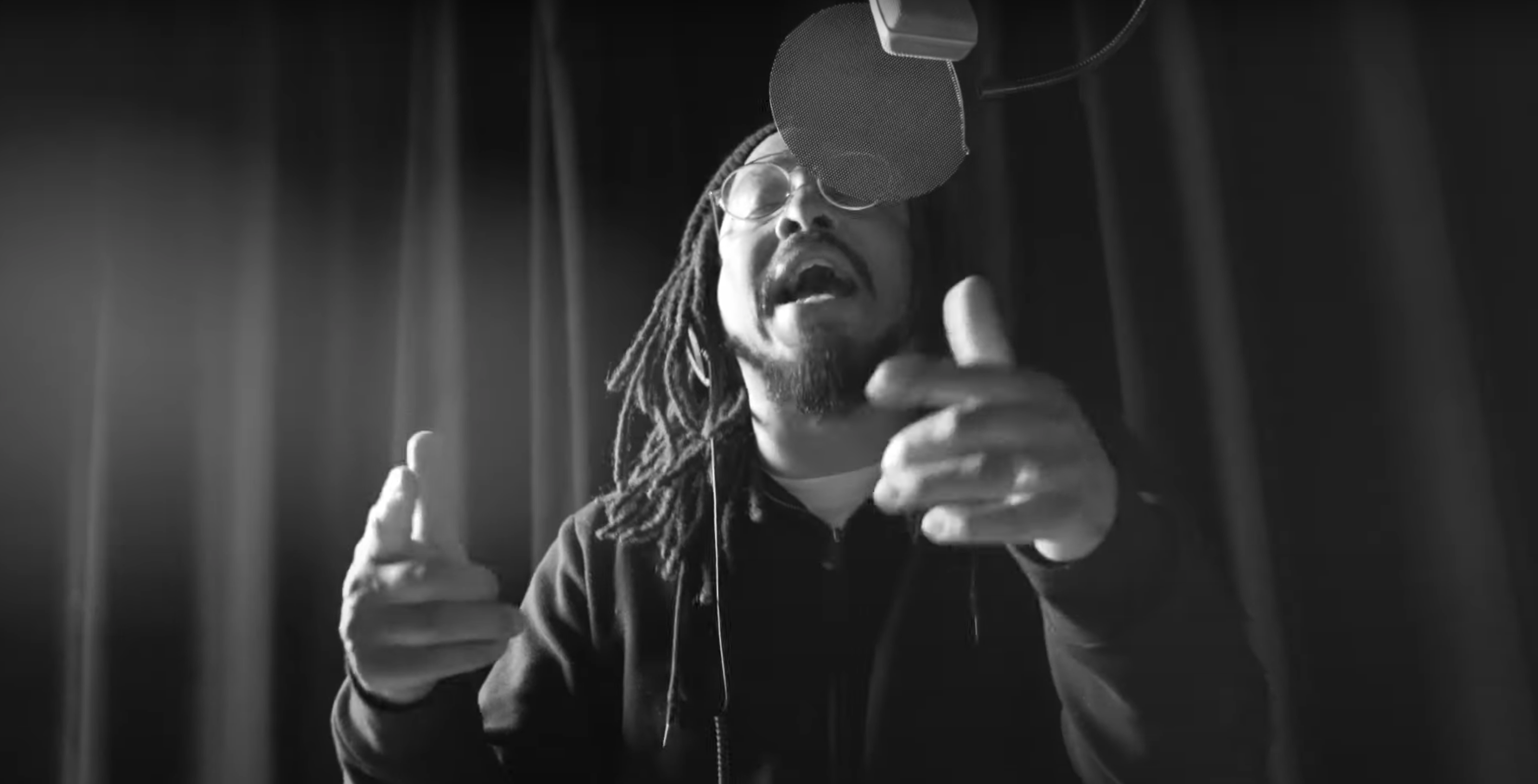 Black and white photo of a man standing in front of a curtain, singing expressively into a microphone with his eyes closed.