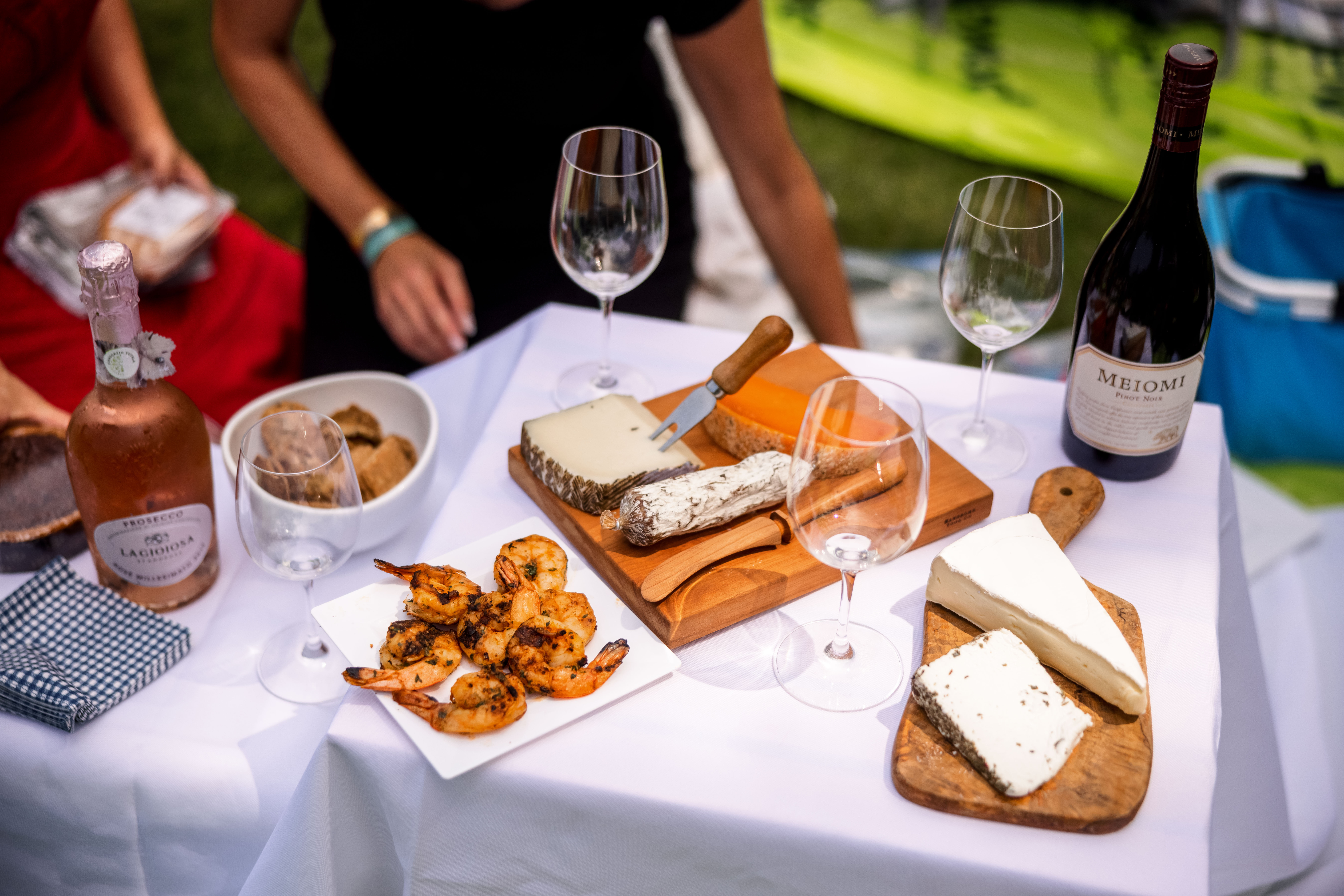 Table covered in white tablecloth with shrimp, wine, and cheese on top