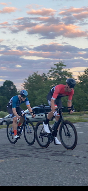 BSO bassist in a red and blue cycling outfit and dark helmet on a bicycle.