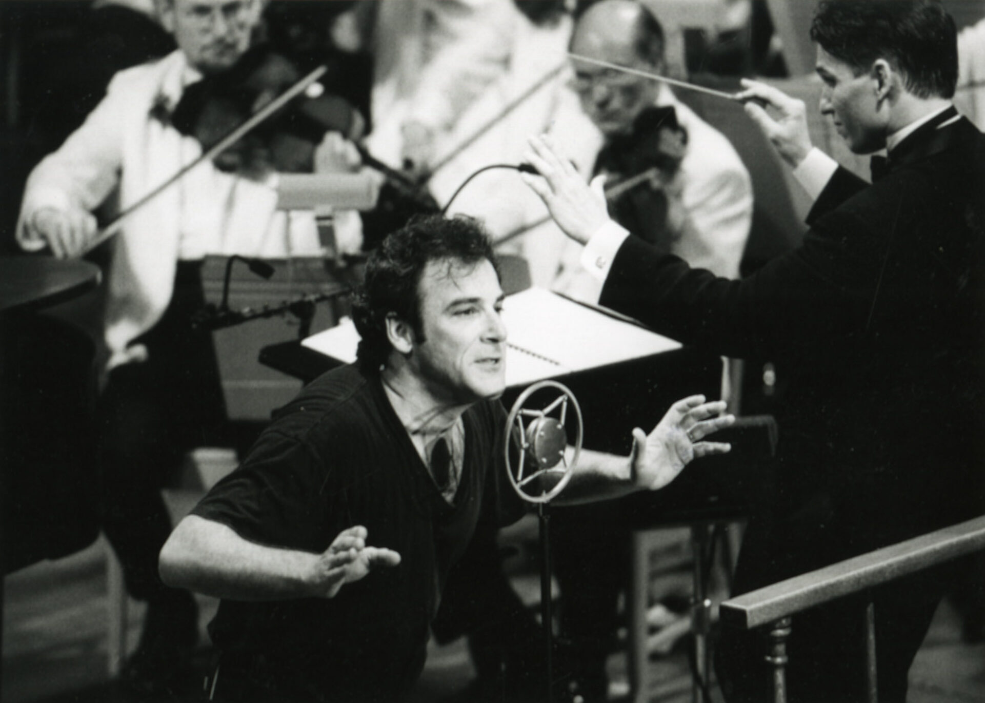 Guest soloist Mandy Patinkin sings into a vintage microphone while Keith Lockhart conducts in the background