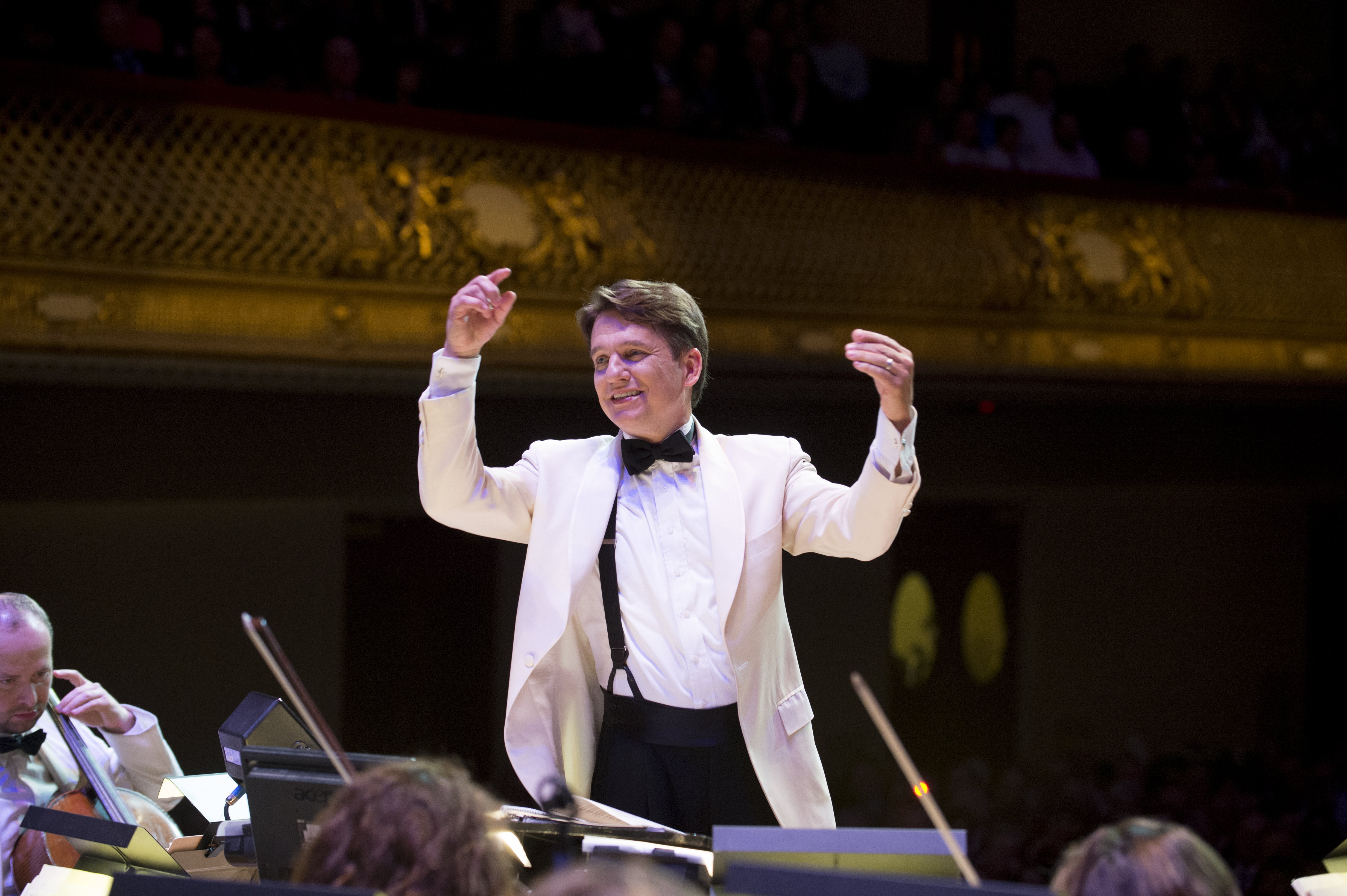 Boston Pops Conductor Keith Lockhart, wearing a white jacket, raises both hands to lead orchestra