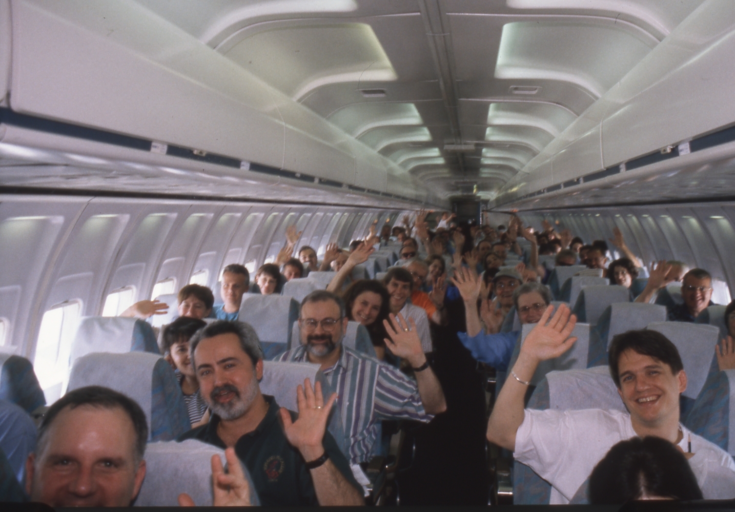 Keith Lockhart and other Pops musicians wave while seated on an airplane, ready to travel on tour in 1999