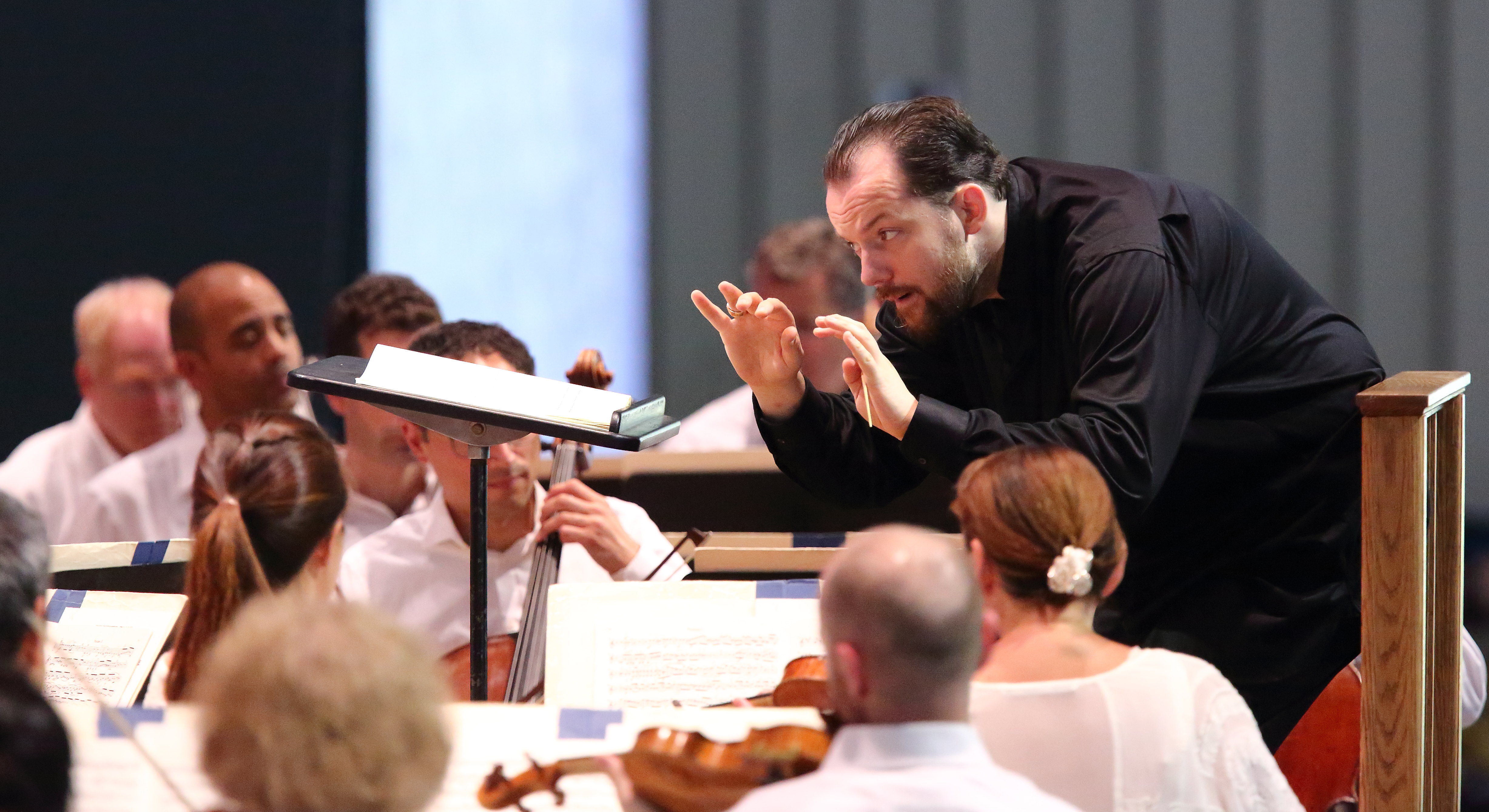 Andris Nelsons leans over his music stand while conducting, eyes wide and his hands close together, as the musicians play