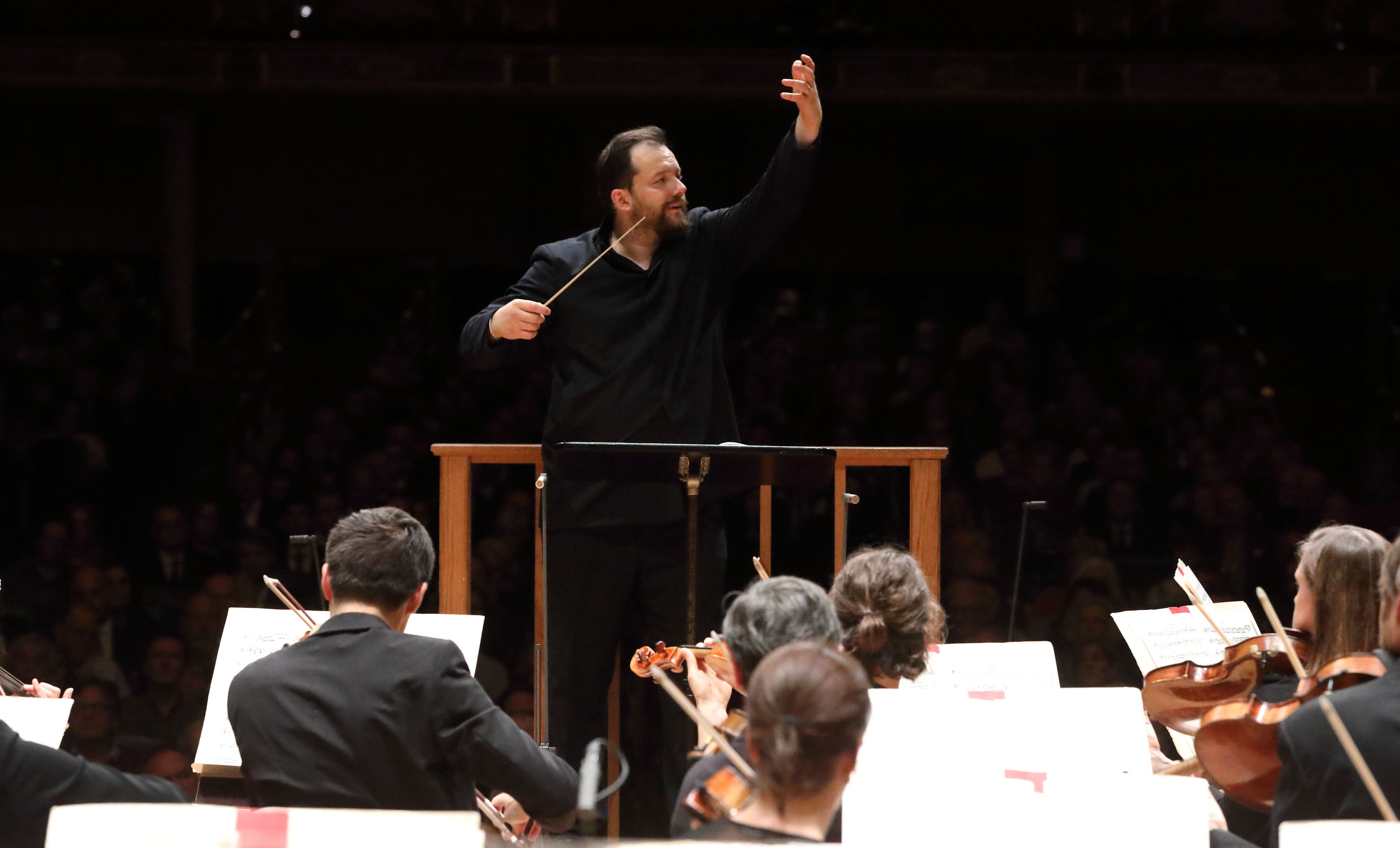 Andris Nelsons is dressed in all black on the Symphony Hall podium, raising his hand high as he conducts the BSO
