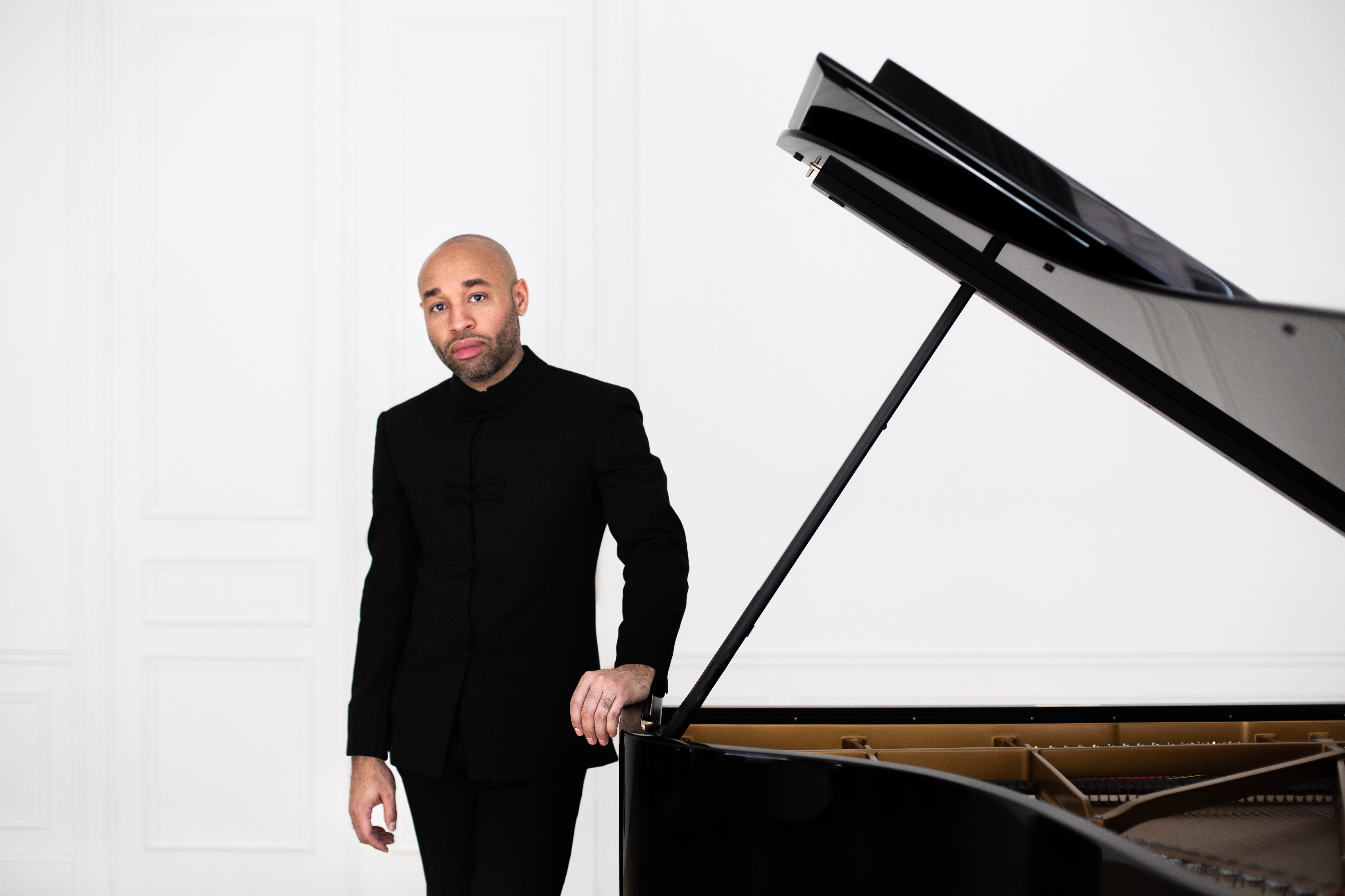 Aaron Diehl dressed in black standing next to a piano with its lid open.