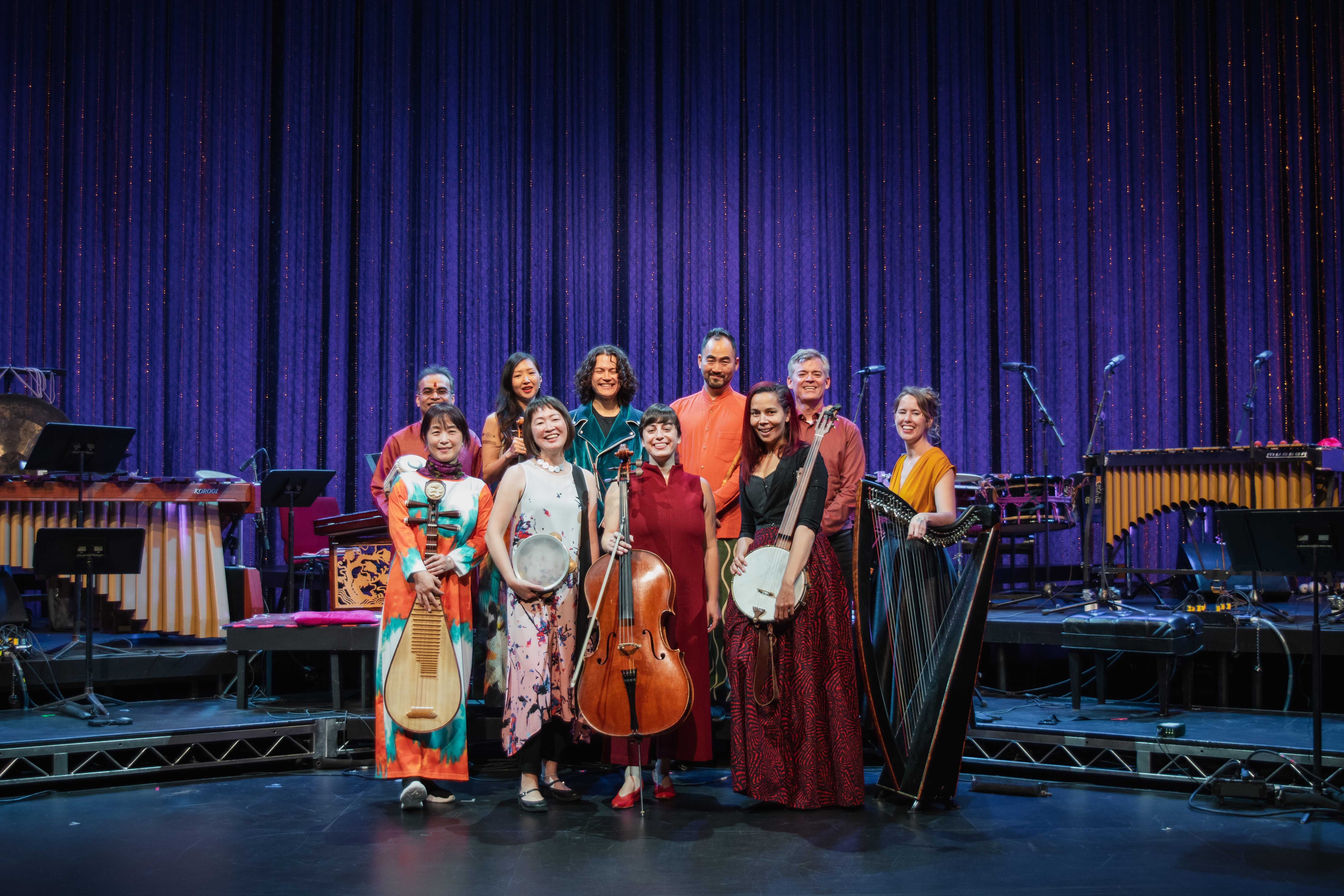 Ten musicians posing onstage with their instruments, dressed in colorful outfits