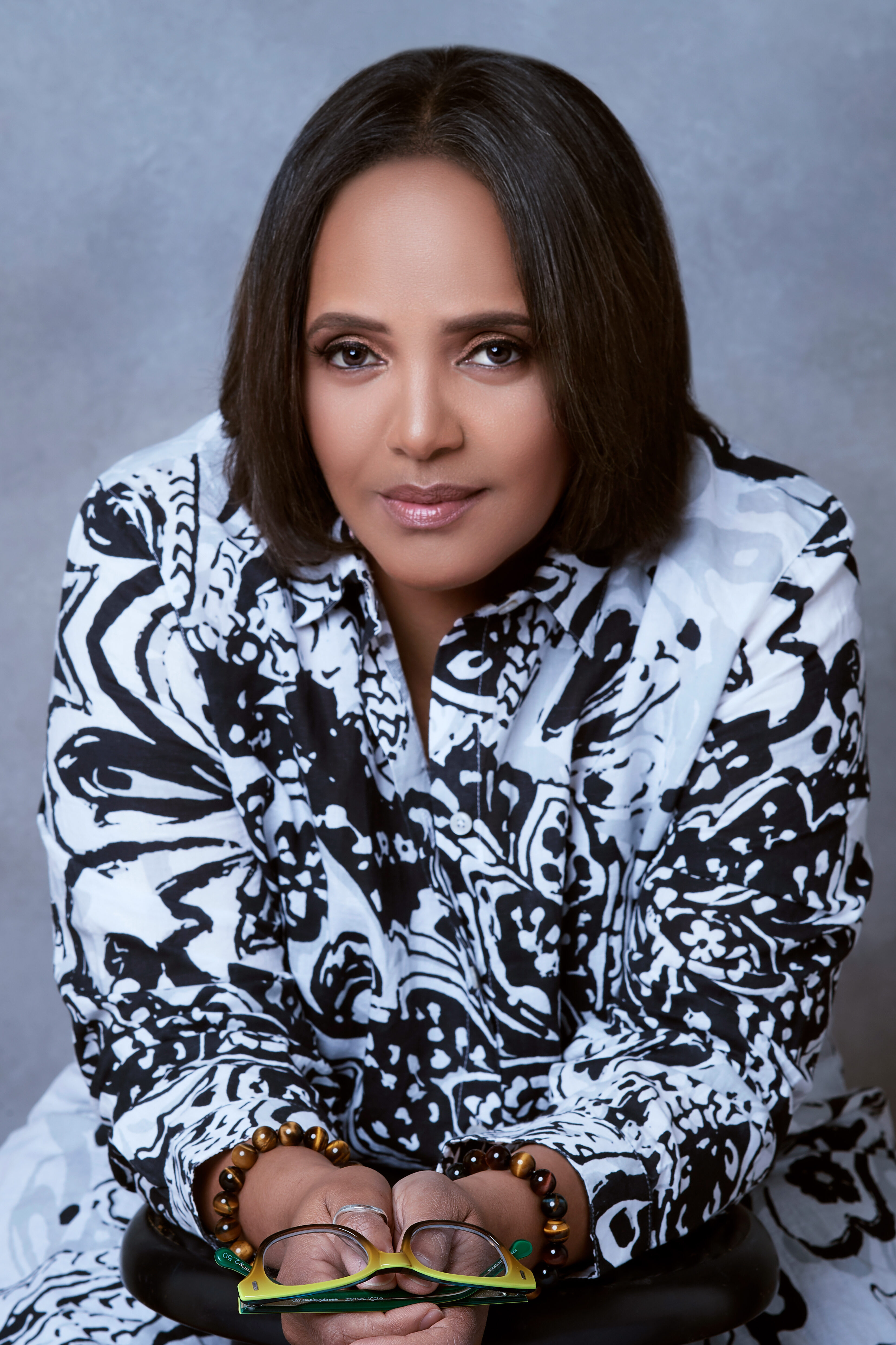 Terri Lyne Carrington leaning forward with her arms resting on a stool, holding a pair of glasses