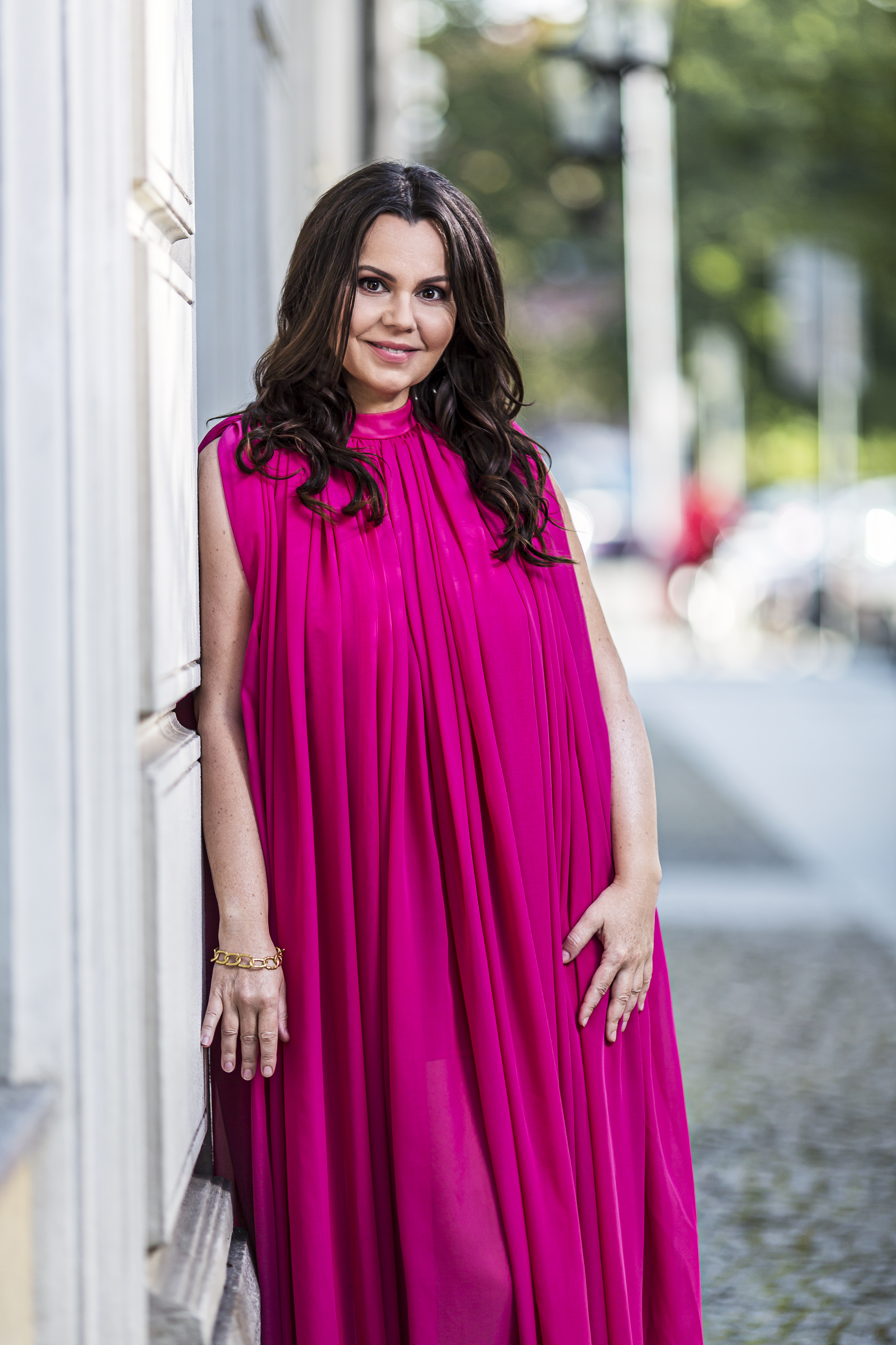 Aleksandra Kurzak leaning against a wall in a bright magenta gown