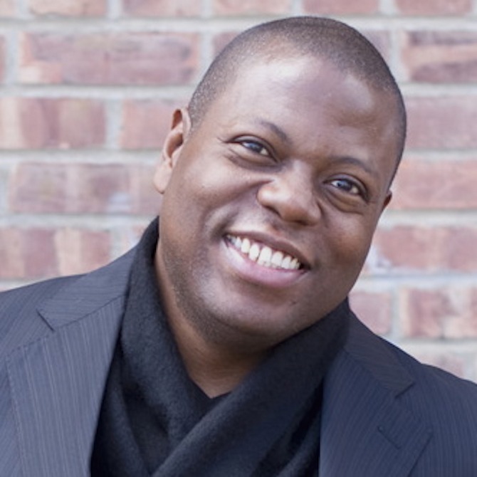 Close-up headshot of Alfred Walker wearing a navy suit jacket and a black scarf