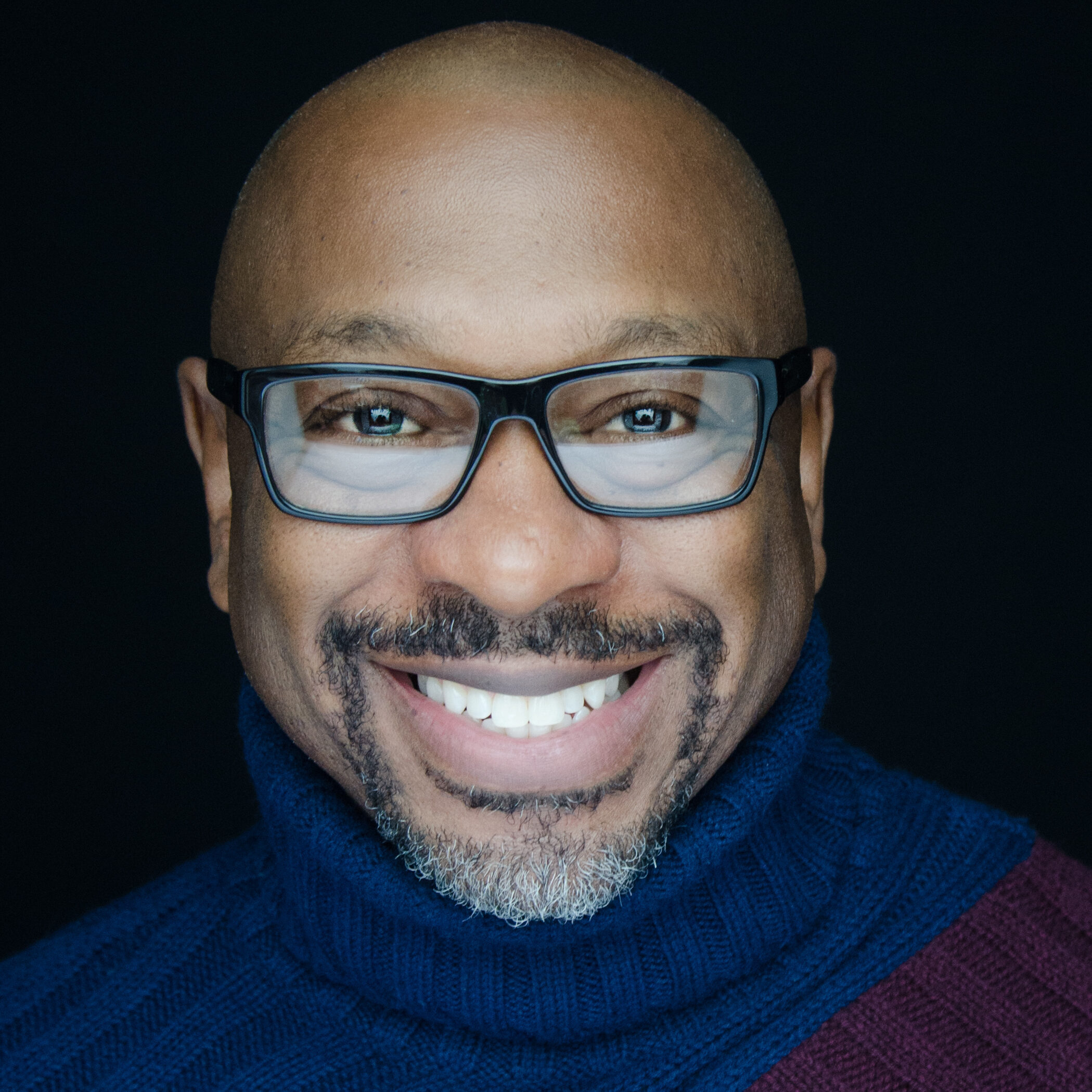 Alton Fitzgerald White smiling wearing glasses and a scarf