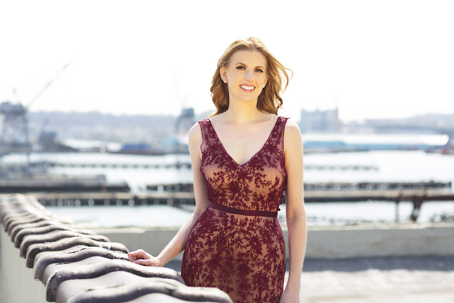 Photo of Amanda Majeski wearing a maroon gown standing outside in front of a body of water
