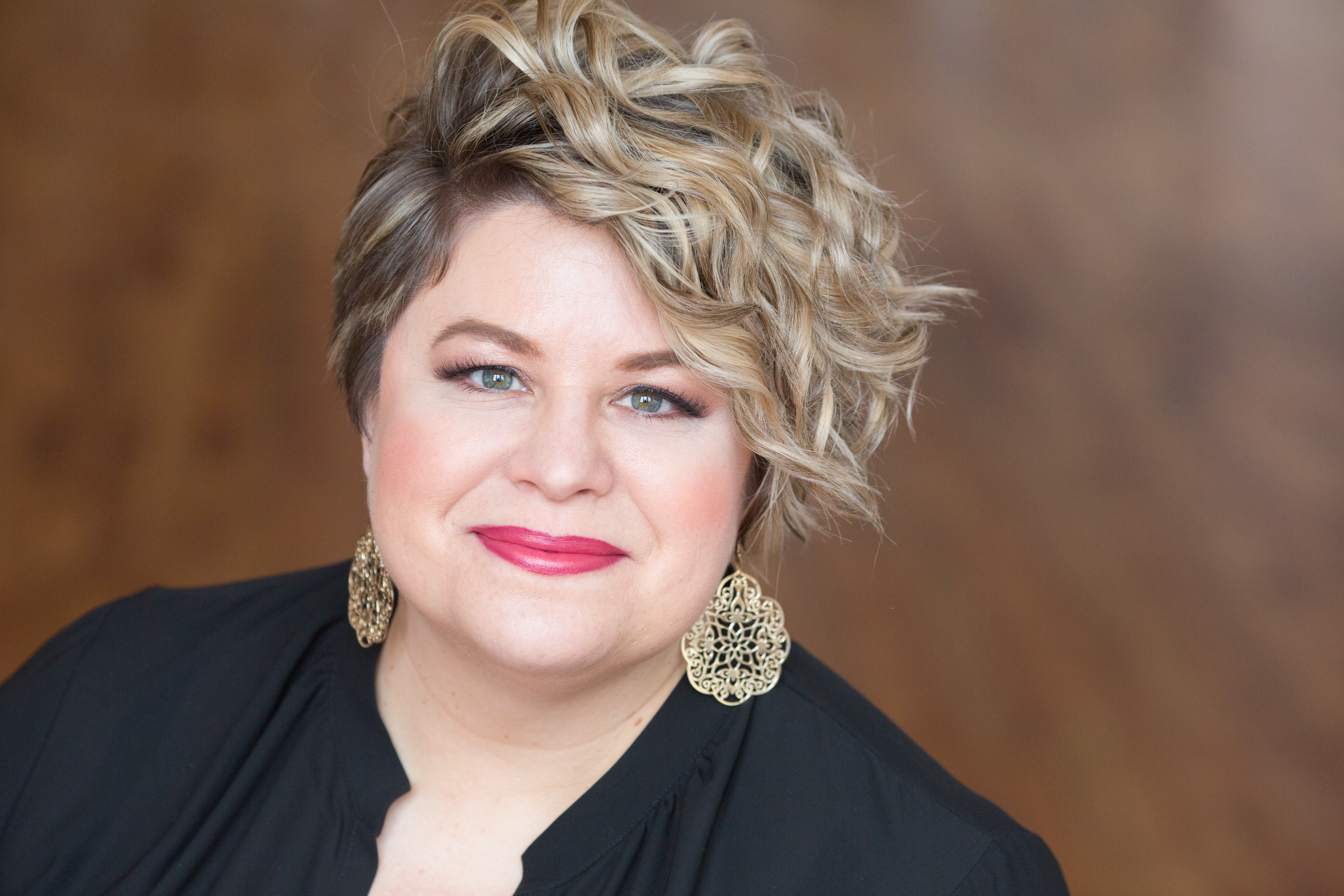 Amber Wagner headshot wearing decorative gold earrings and a black top