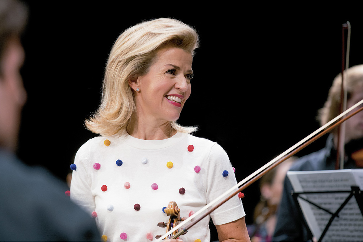 portrait of Ann Sophie Mutter holding her violin while wearing a white top with multicolored plush dots