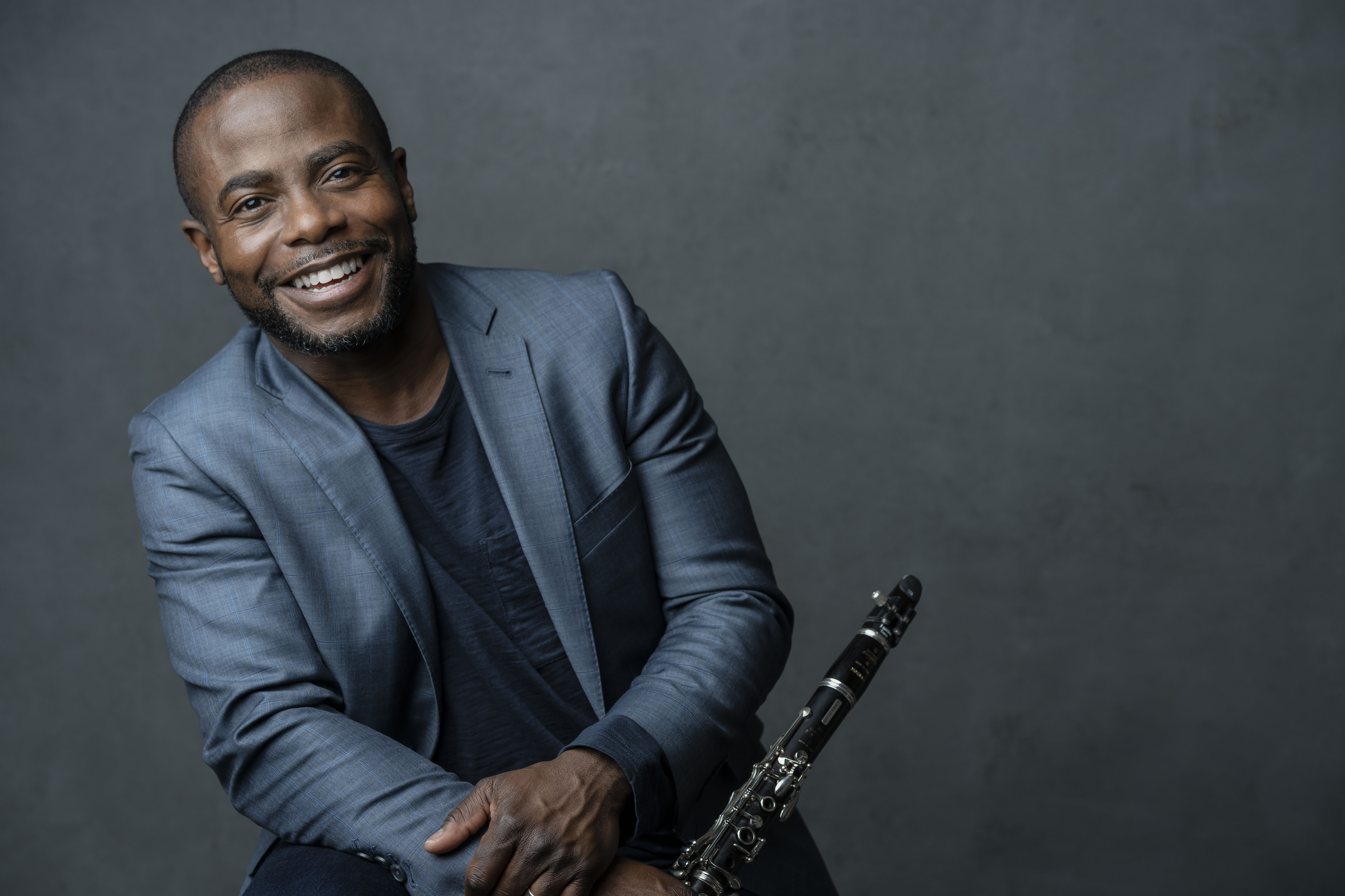 Anthony McGill holding a clarinet and smiling in front of a gray background