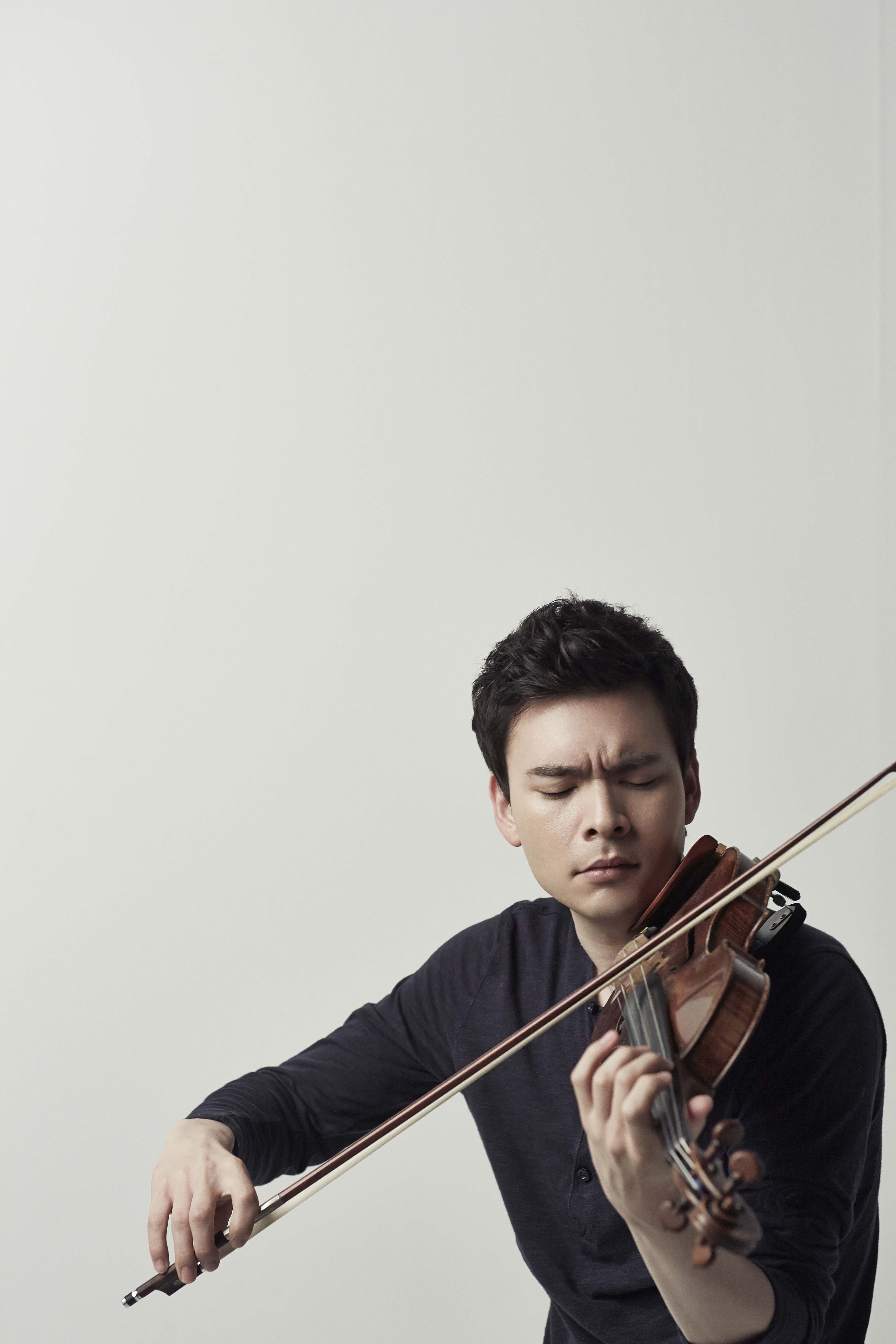 Stefan Jackiw playing a violin against a beige background