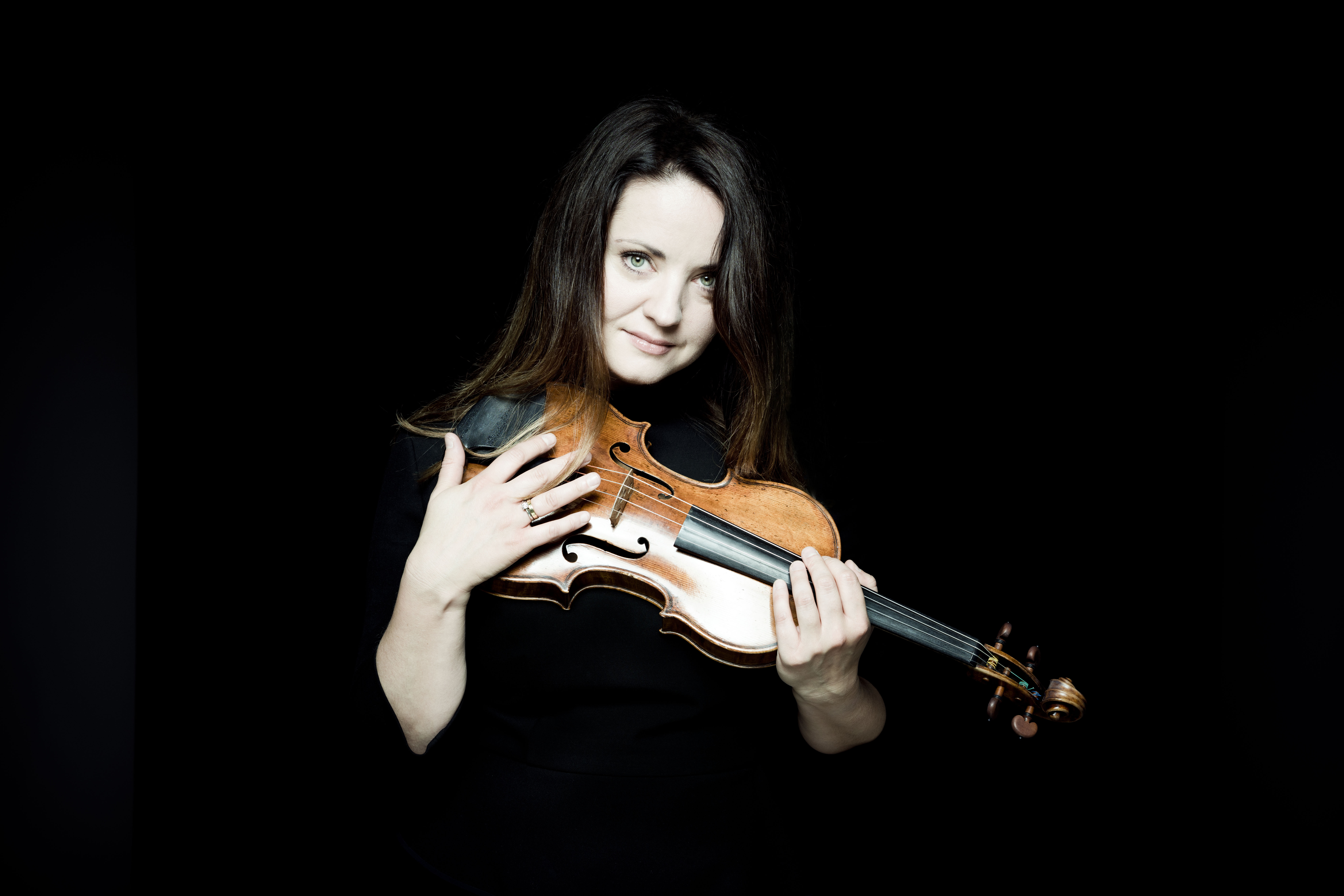 Portrait of Baiba Skride holding her violin in front of a black background