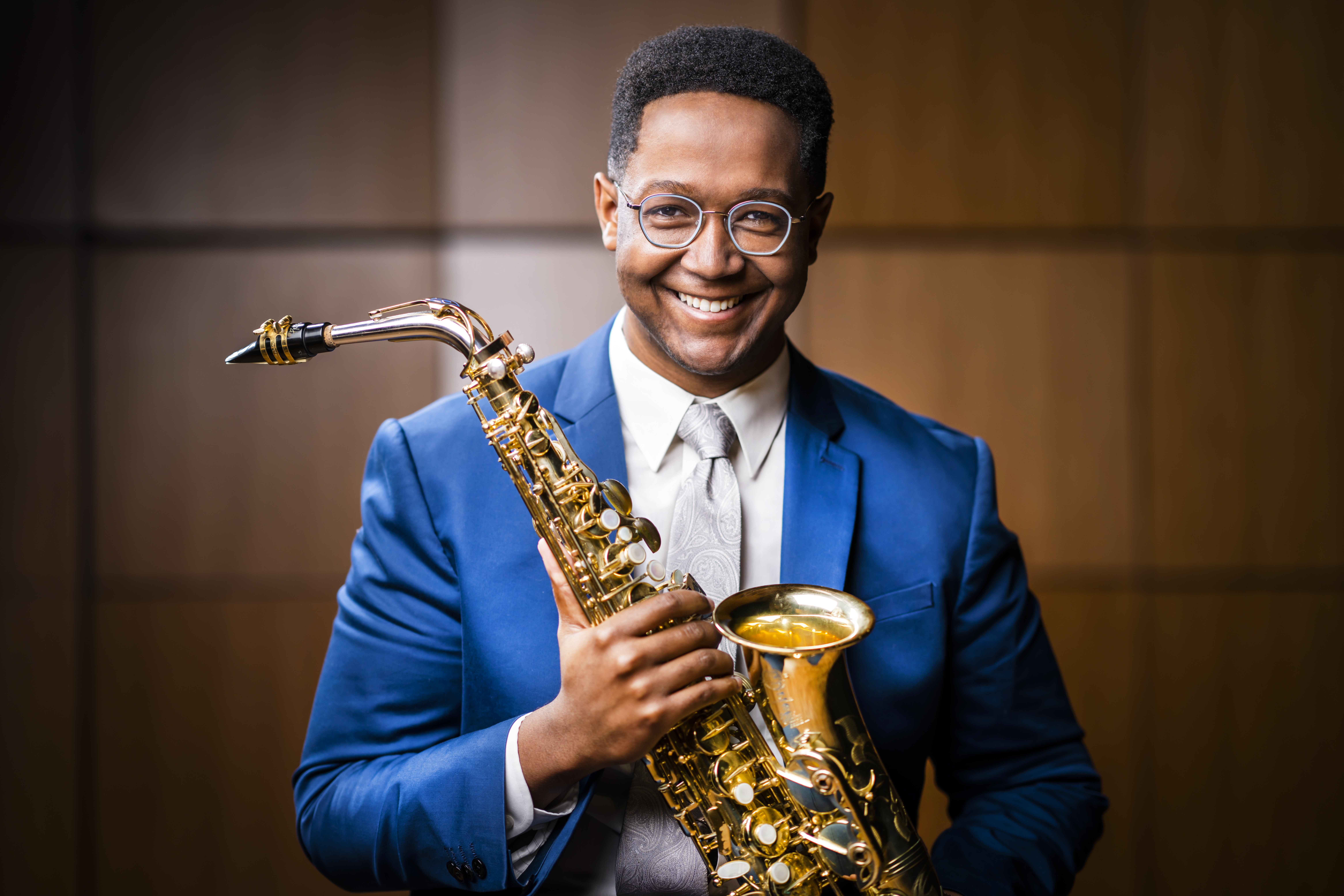 A headshot of Steven Banks wearing a blue suit and holding a saxophone