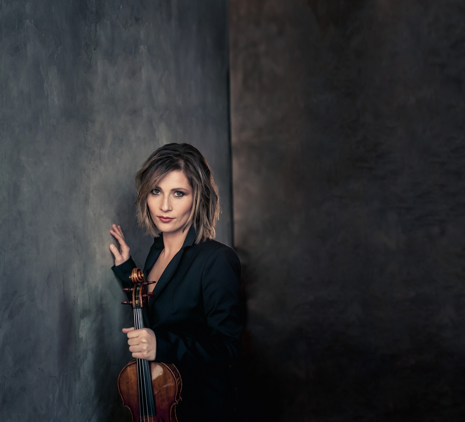 Lisa Batiashvili standing by a wall, holding her violin in front of her