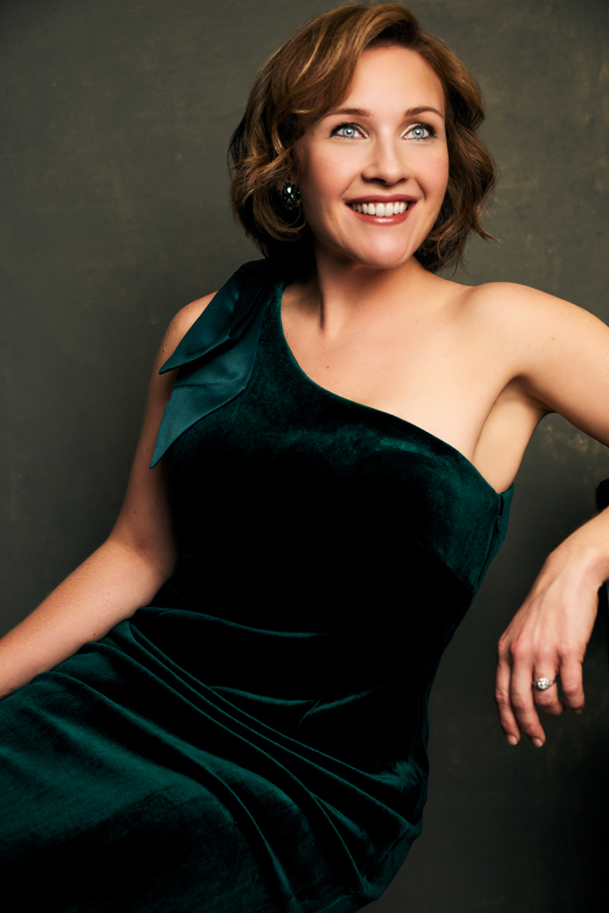 portrait of Sasha Cooke, wearing a velvet green evening gown, leaving back and smiling