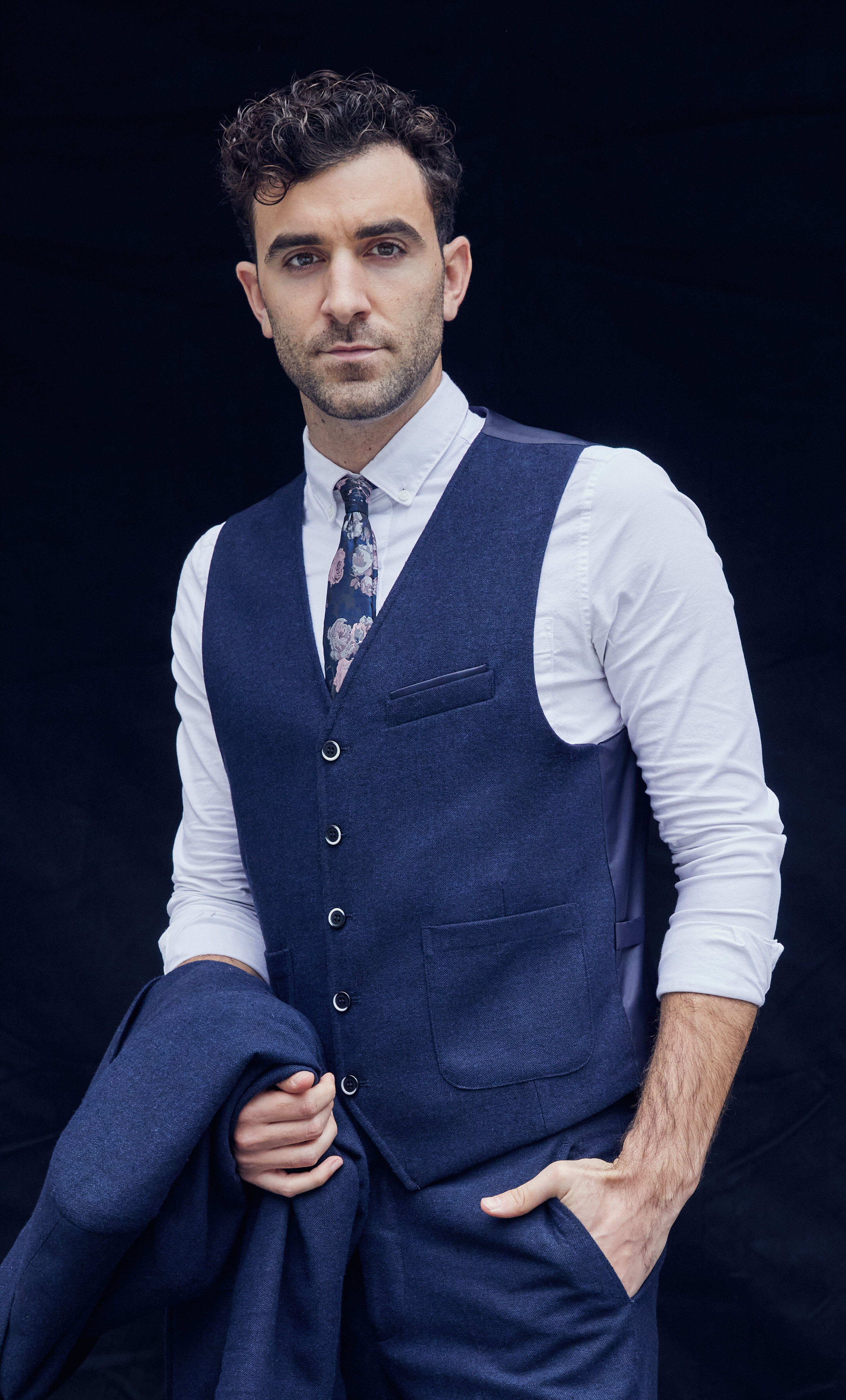 Adam J Levy wearing a blue 3-piece suit with the jacket folded over his arm