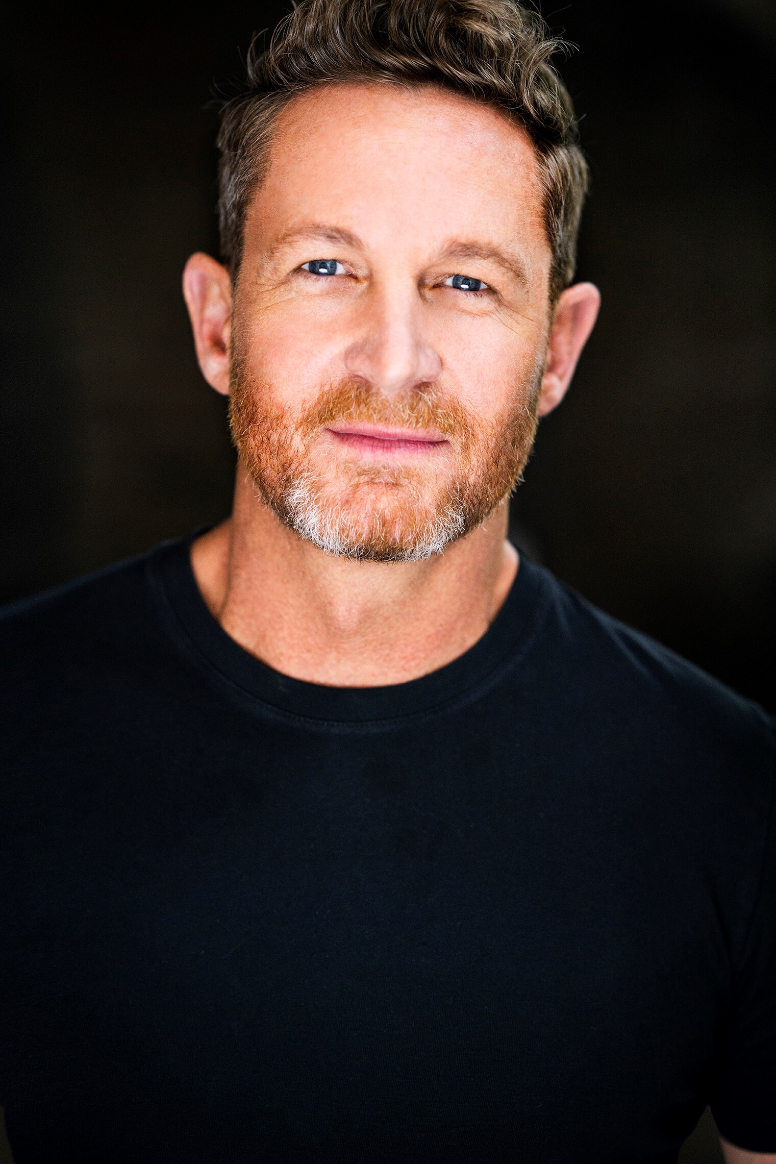 A headshot of David Harris wearing a black crew neck standing against a black background
