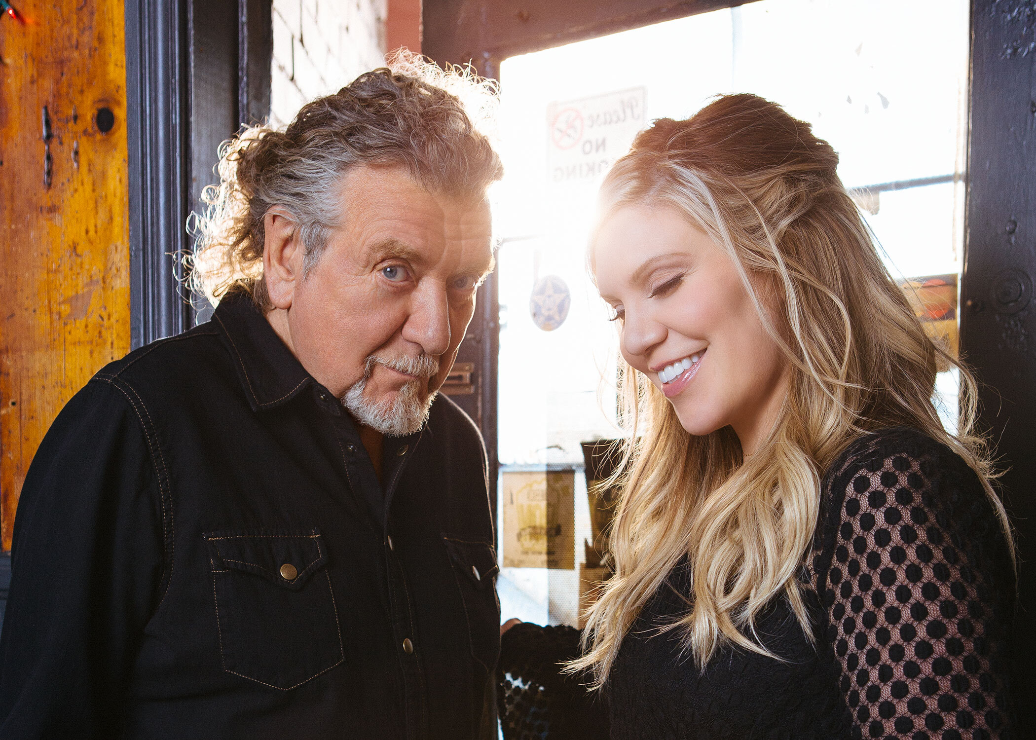 Robert Plant and Alison Krauss standing in front of a window, smiling