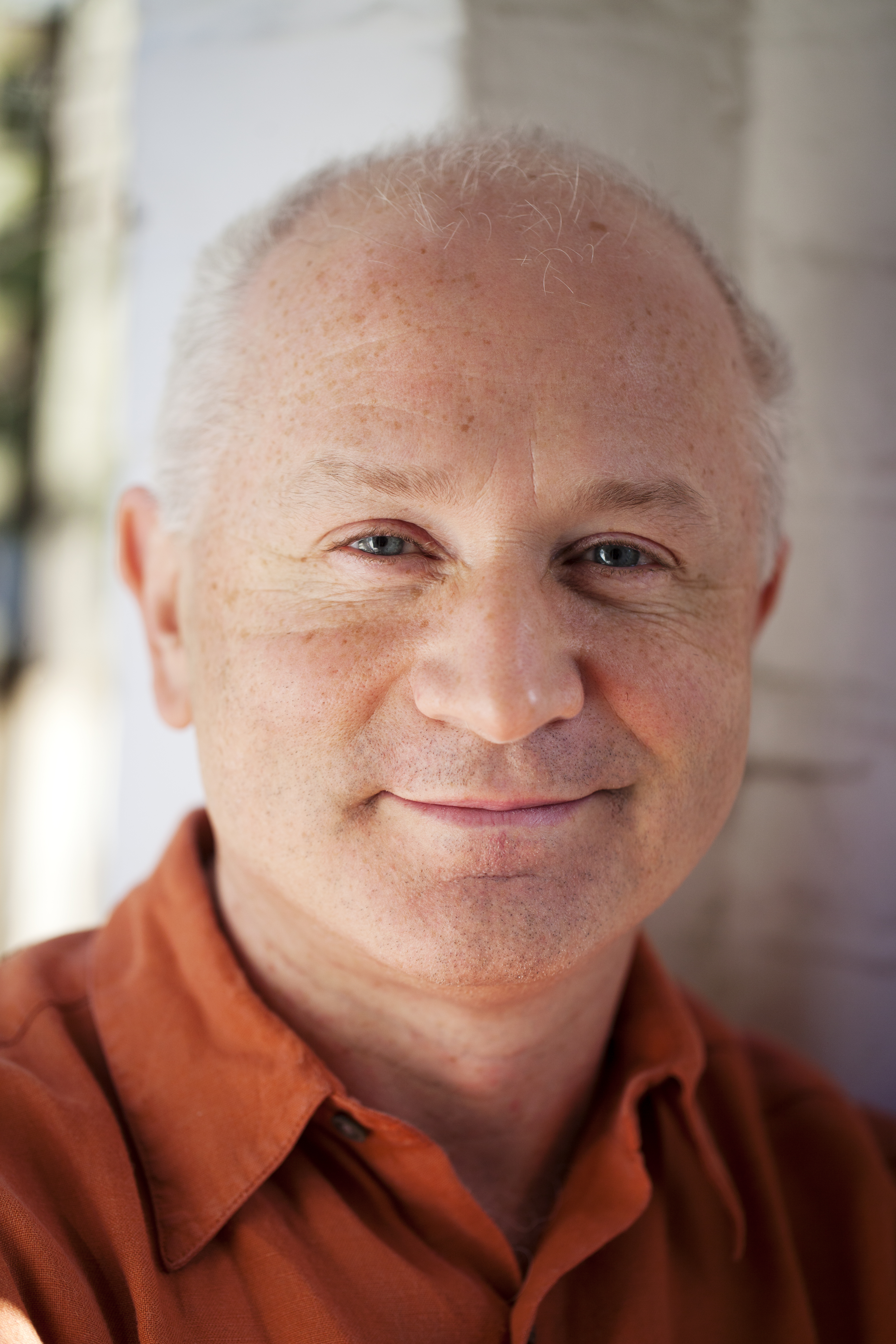 Headshot of George Benjamin wearing an orange collared shirt